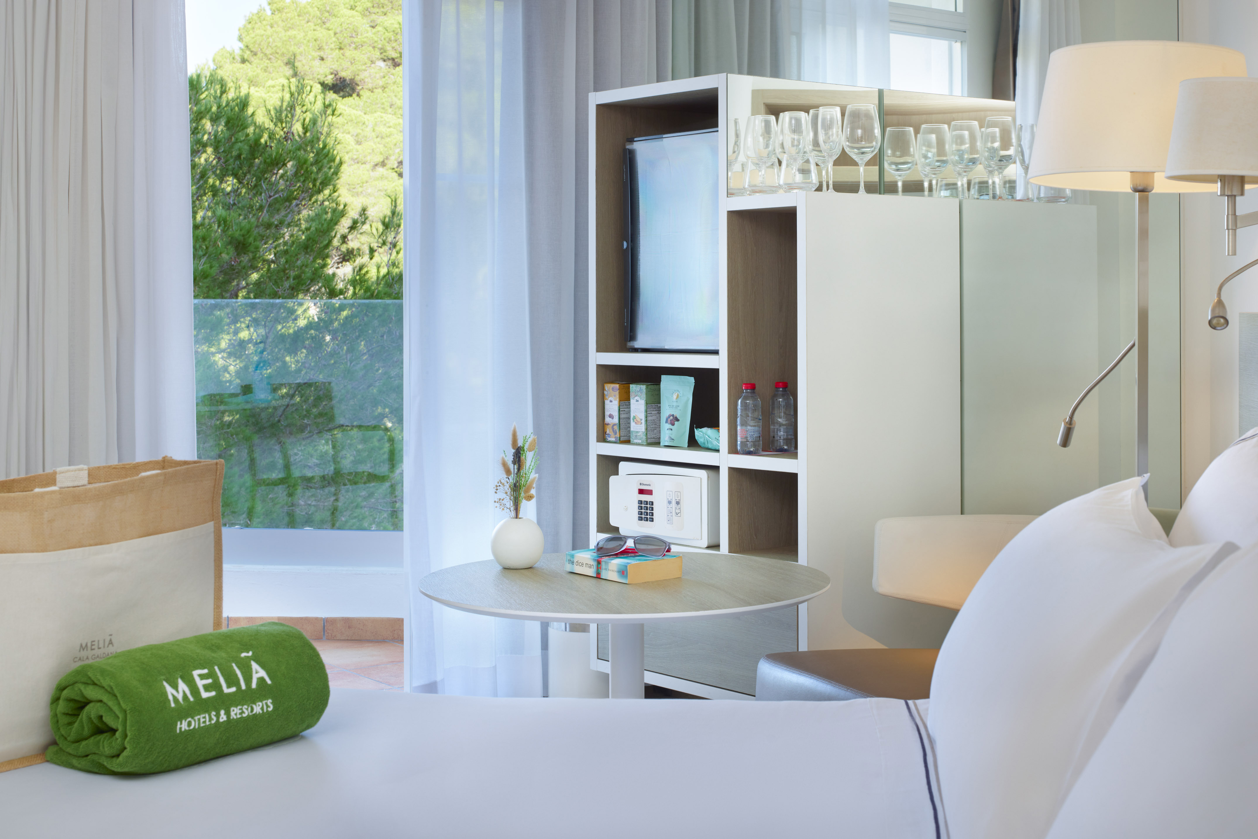 Modern Meliá hotel room with white bed, minibar, and green balcony view.