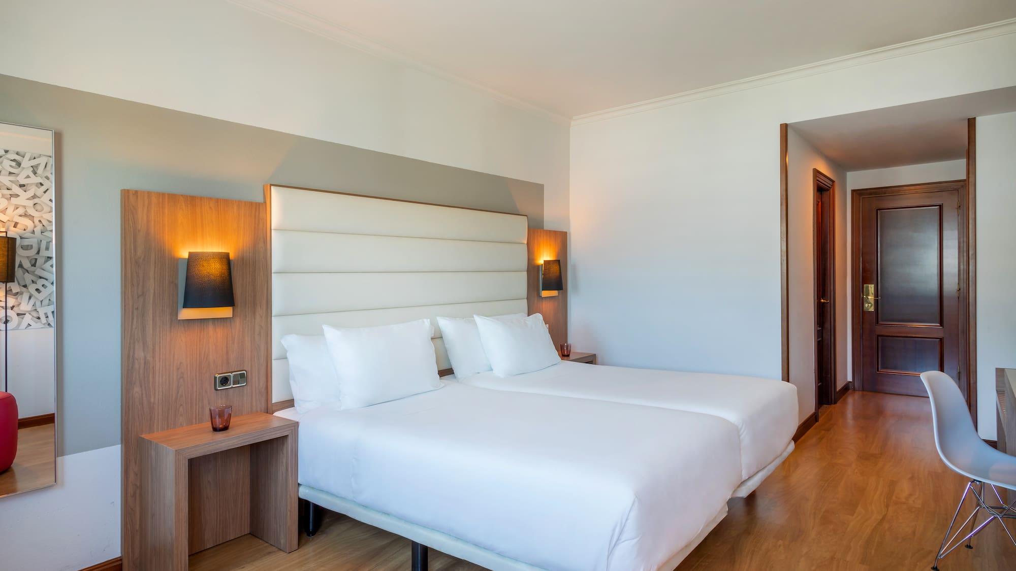 Bright hotel bedroom with twin beds, white linens, wood accents, and modern design.