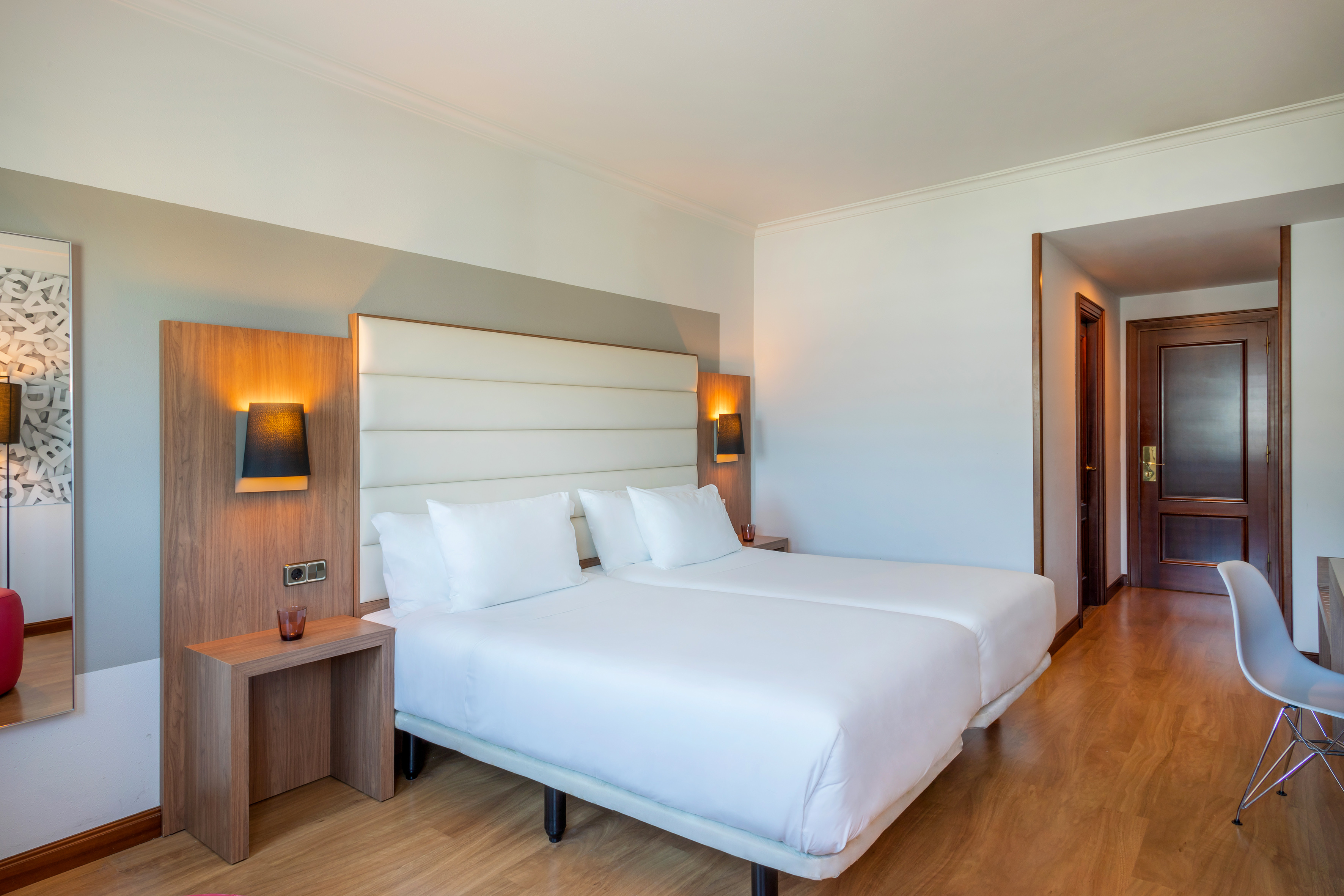 Bright hotel bedroom with twin beds, white linens, wood accents, and modern design.