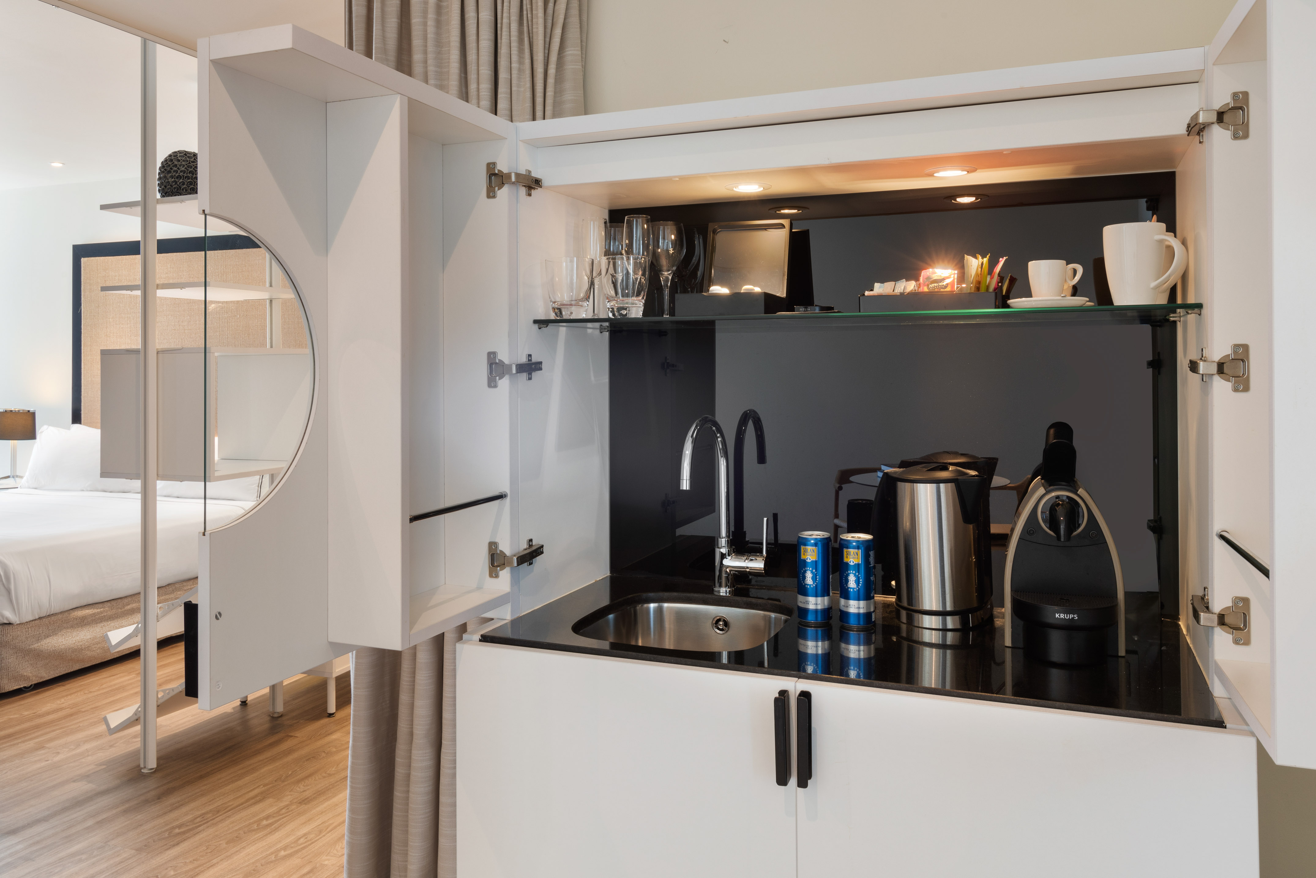 Compact hotel kitchenette with sink, Krups coffee machine, kettle, and glassware.
