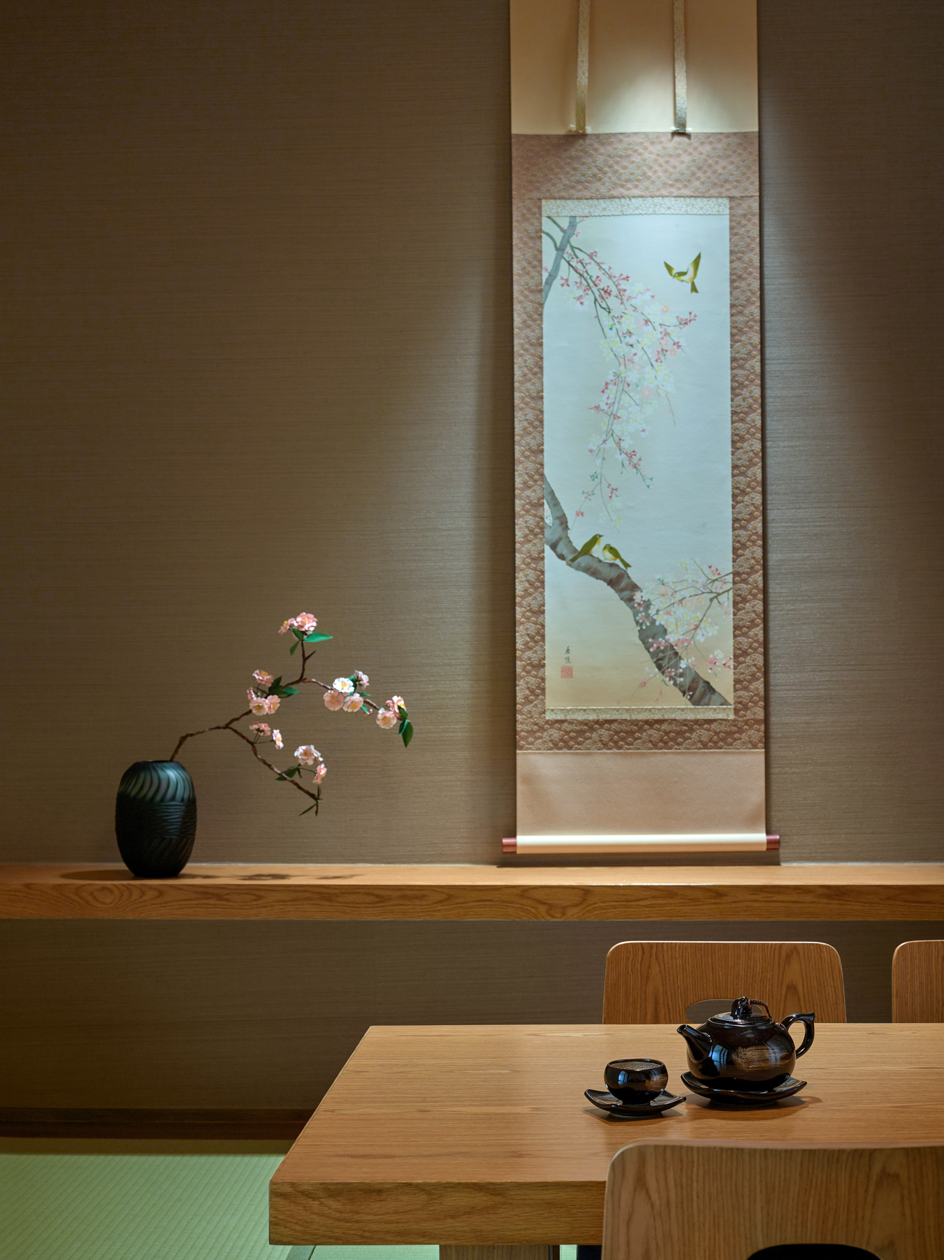 Japanese room with sakura scroll painting, dark teapot set, and cherry blossom vase.
