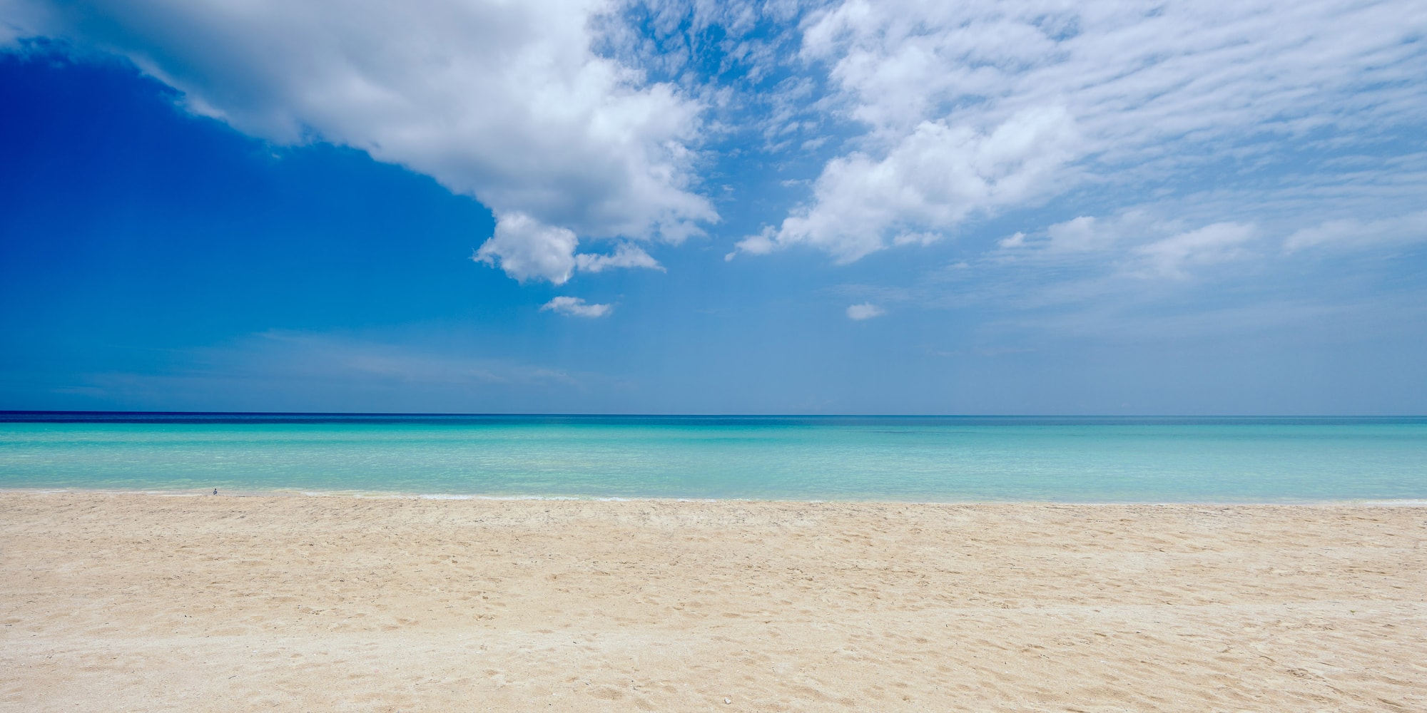 a sandy beach with blue water and clouds in the sky