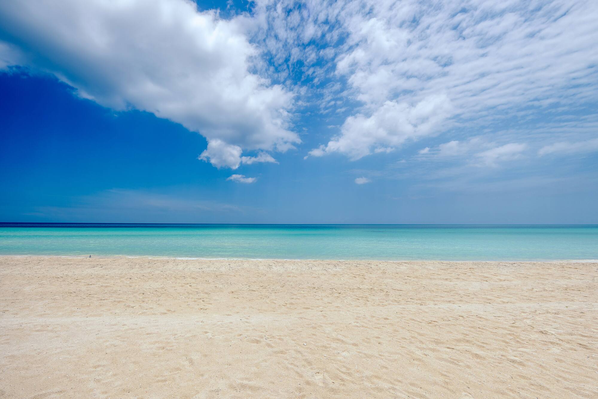 a sandy beach with blue water and clouds in the sky