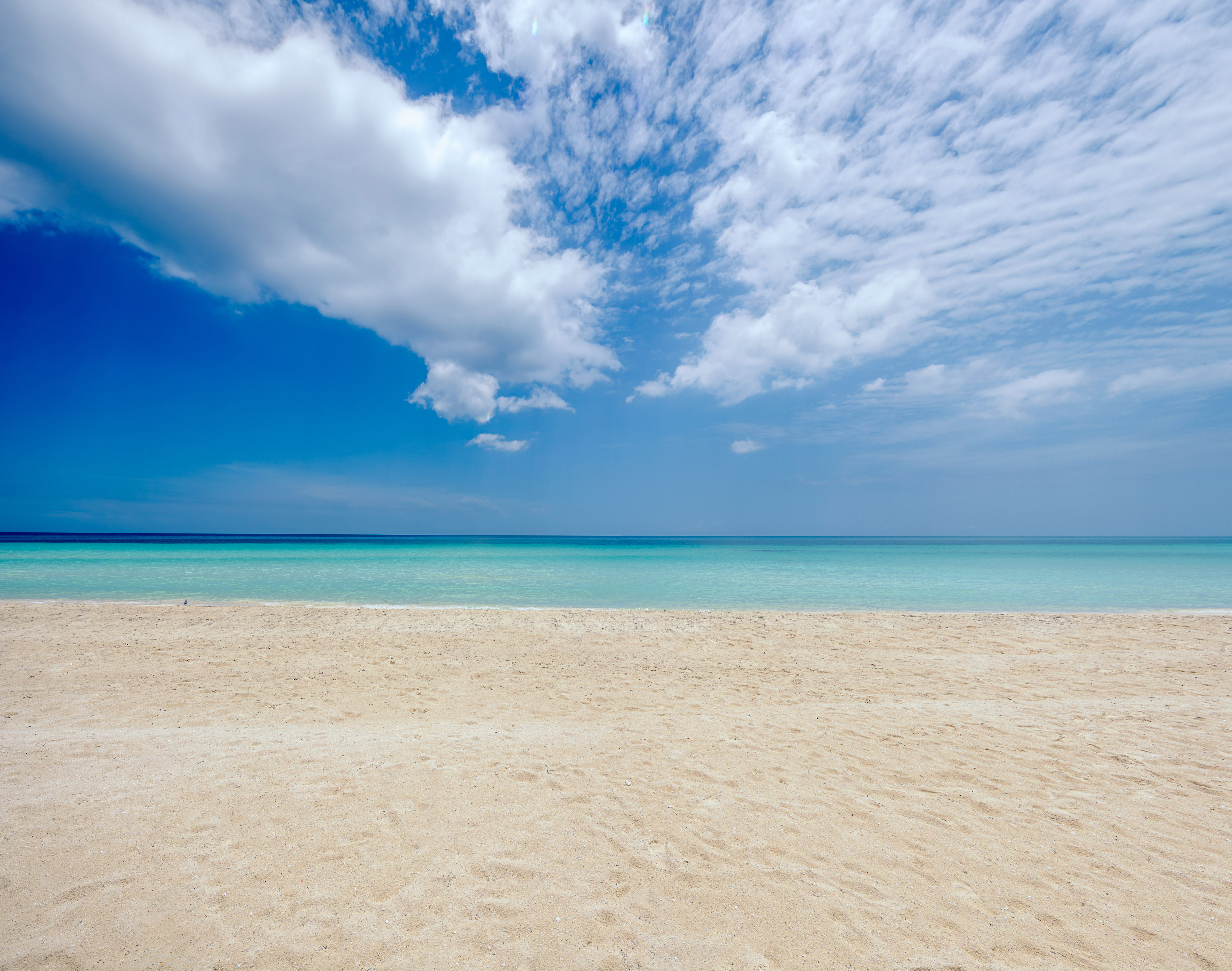 a sandy beach with blue water and clouds in the sky