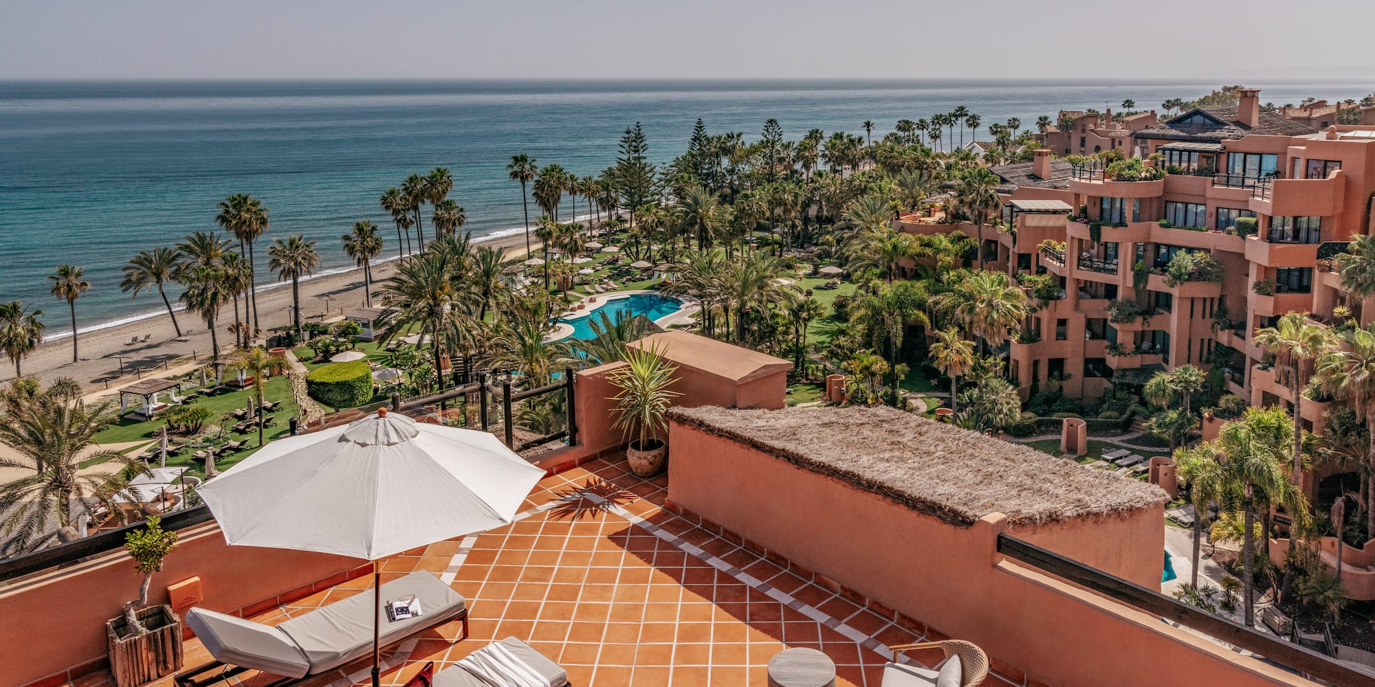 Rooftop terrace with ocean, beach, palm trees, and luxury resort view.