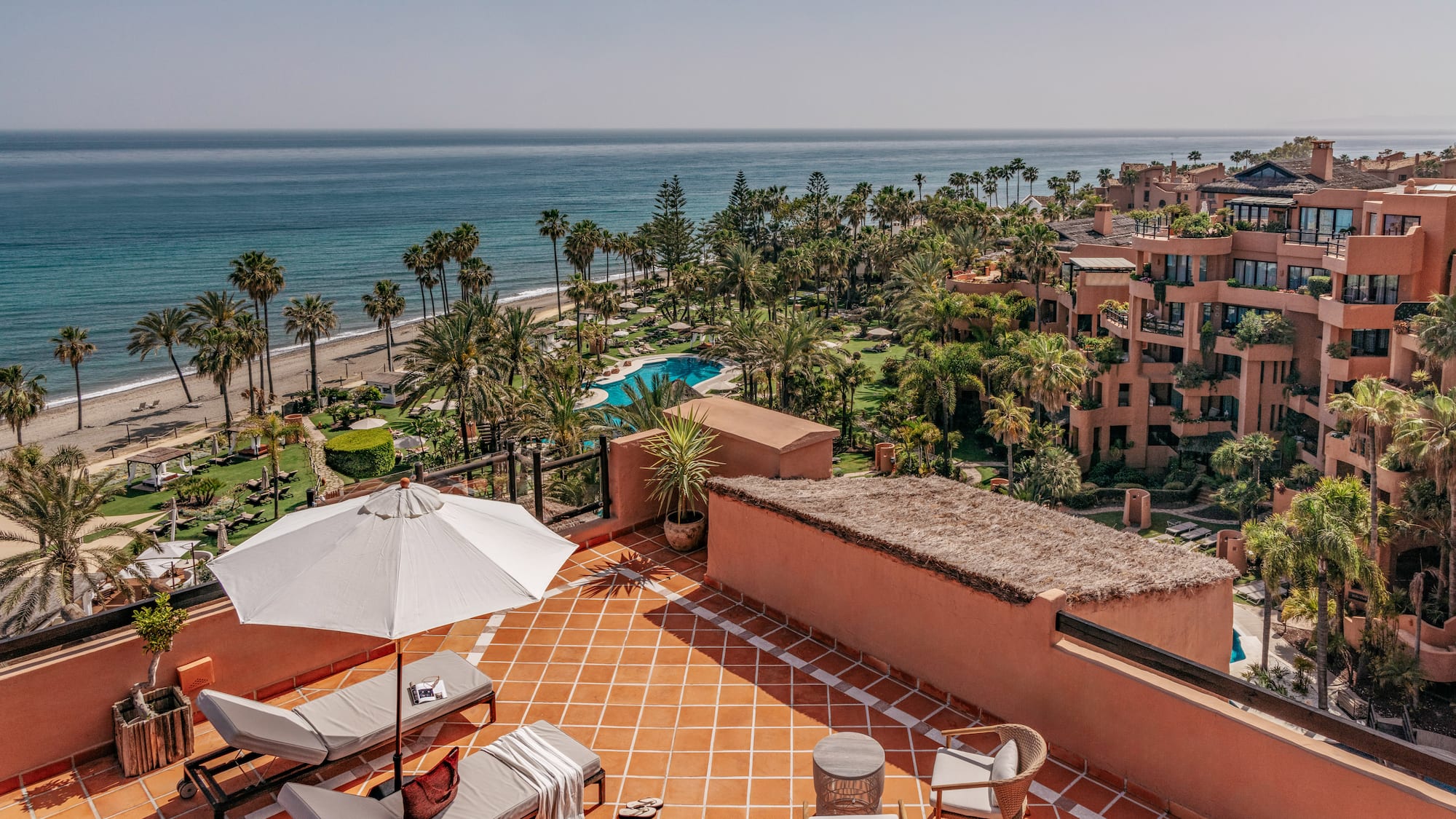 Rooftop terrace with ocean, beach, palm trees, and luxury resort view.