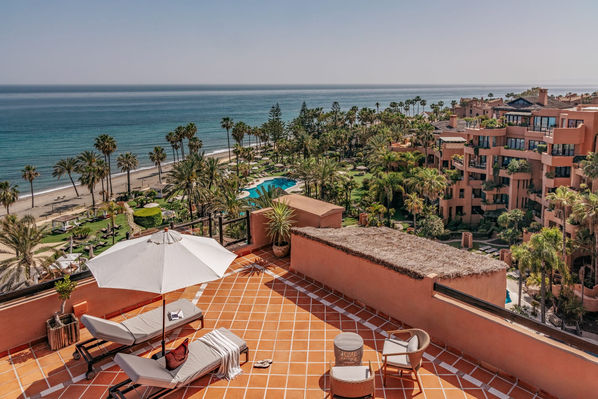 Rooftop terrace with ocean, beach, palm trees, and luxury resort view.
