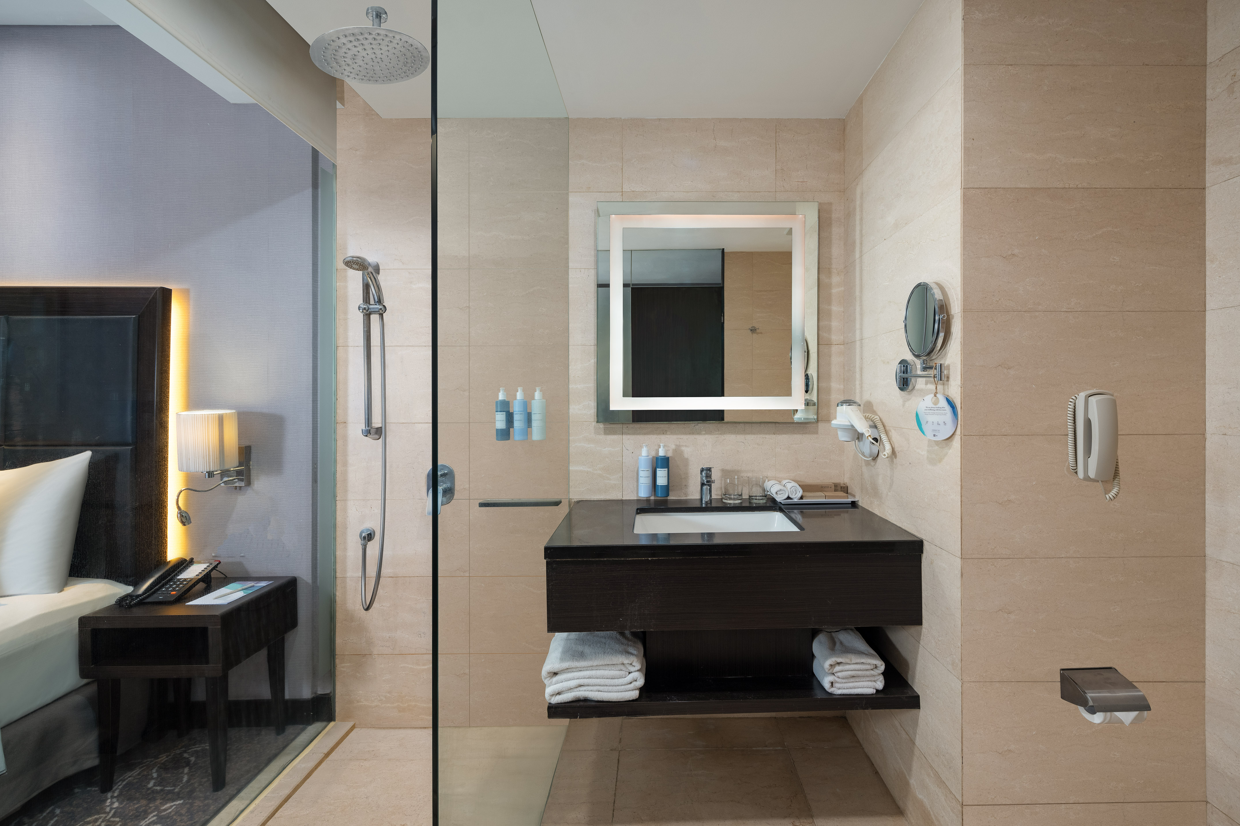 Modern hotel bathroom with glass shower, lit mirror, and vanity.