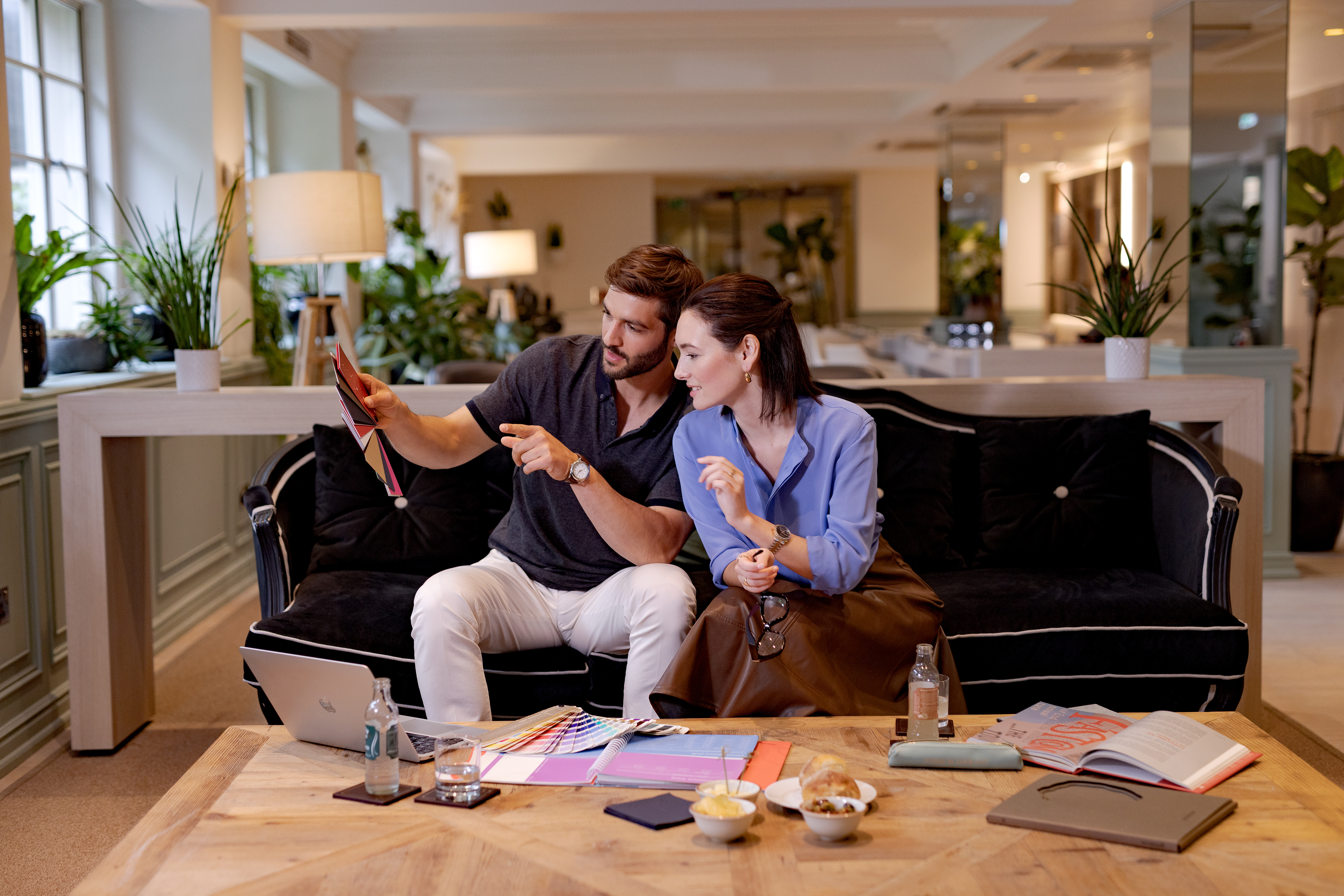 a man and woman sitting on a couch looking at a color swatch