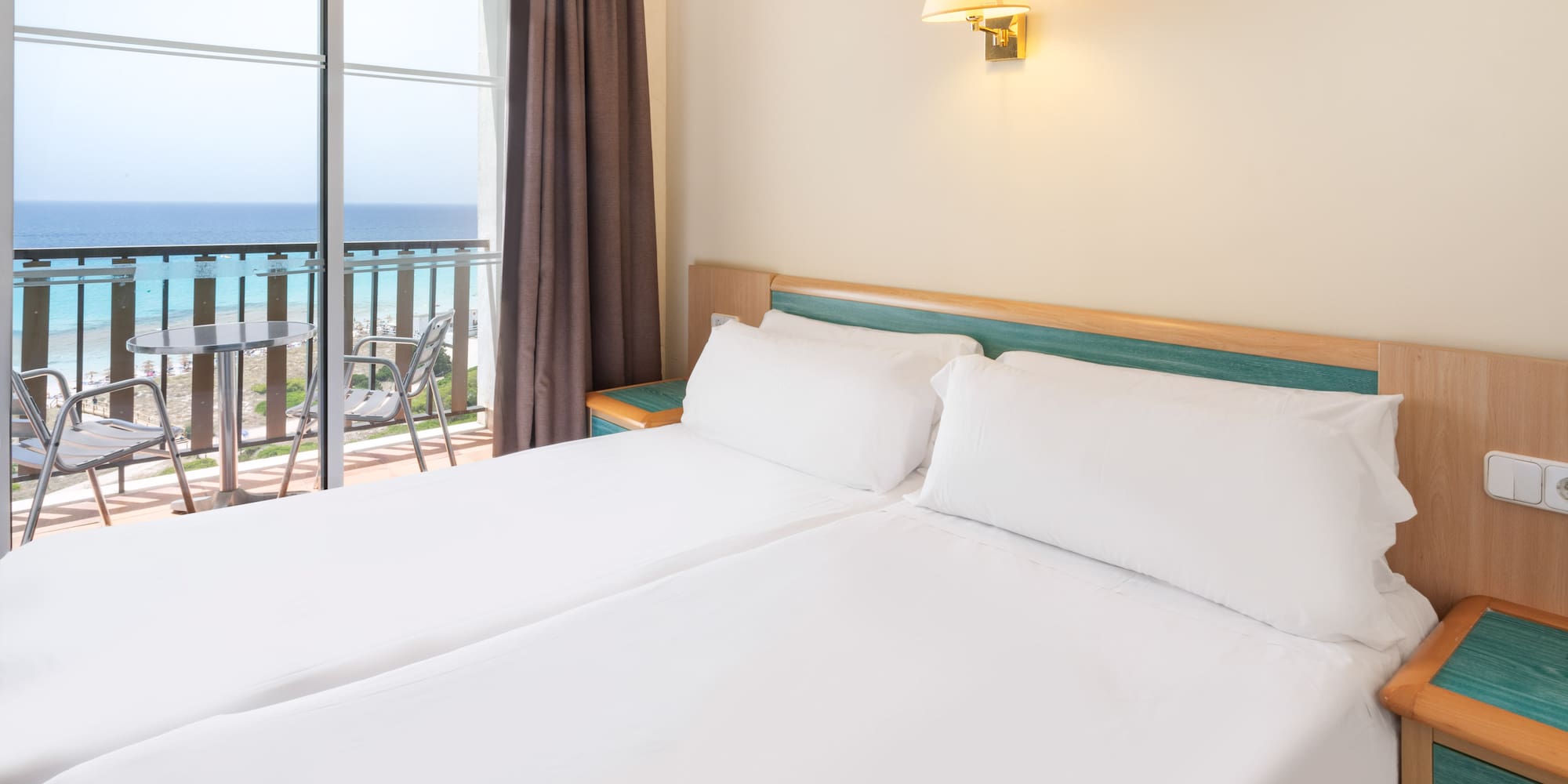 a bed with white sheets and a window with a balcony overlooking the ocean