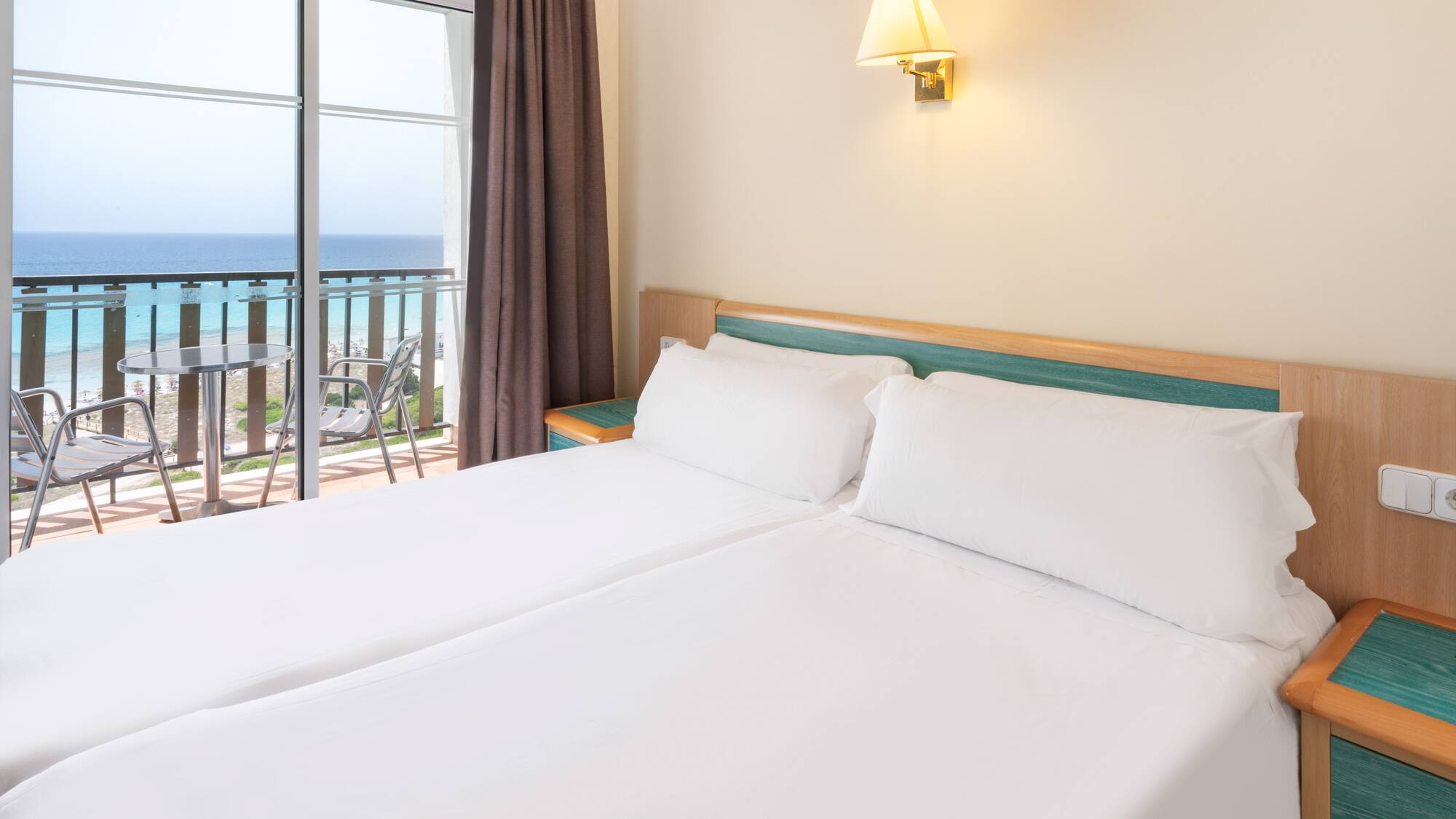 a bed with white sheets and a window with a balcony overlooking the ocean