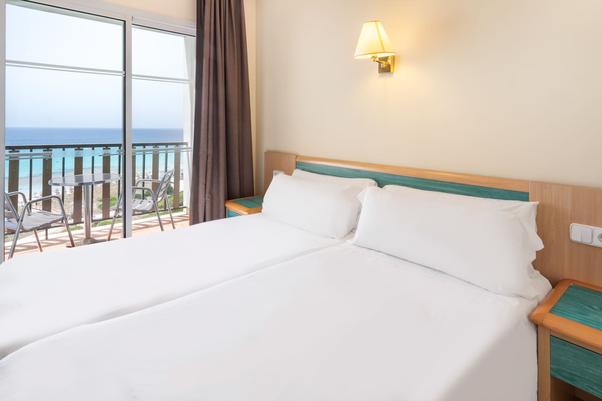 a bed with white sheets and a window with a balcony overlooking the ocean