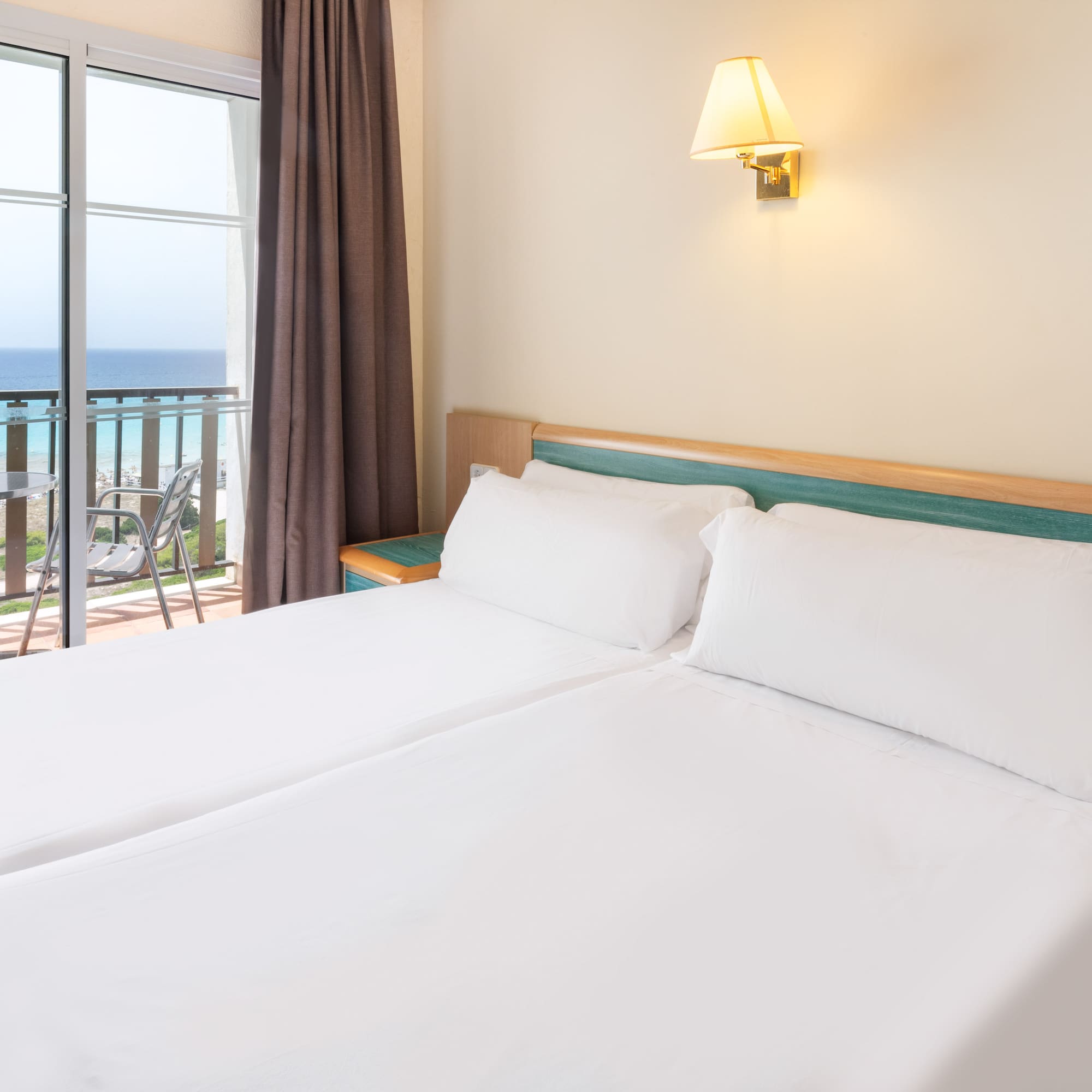 a bed with white sheets and a window with a balcony overlooking the ocean