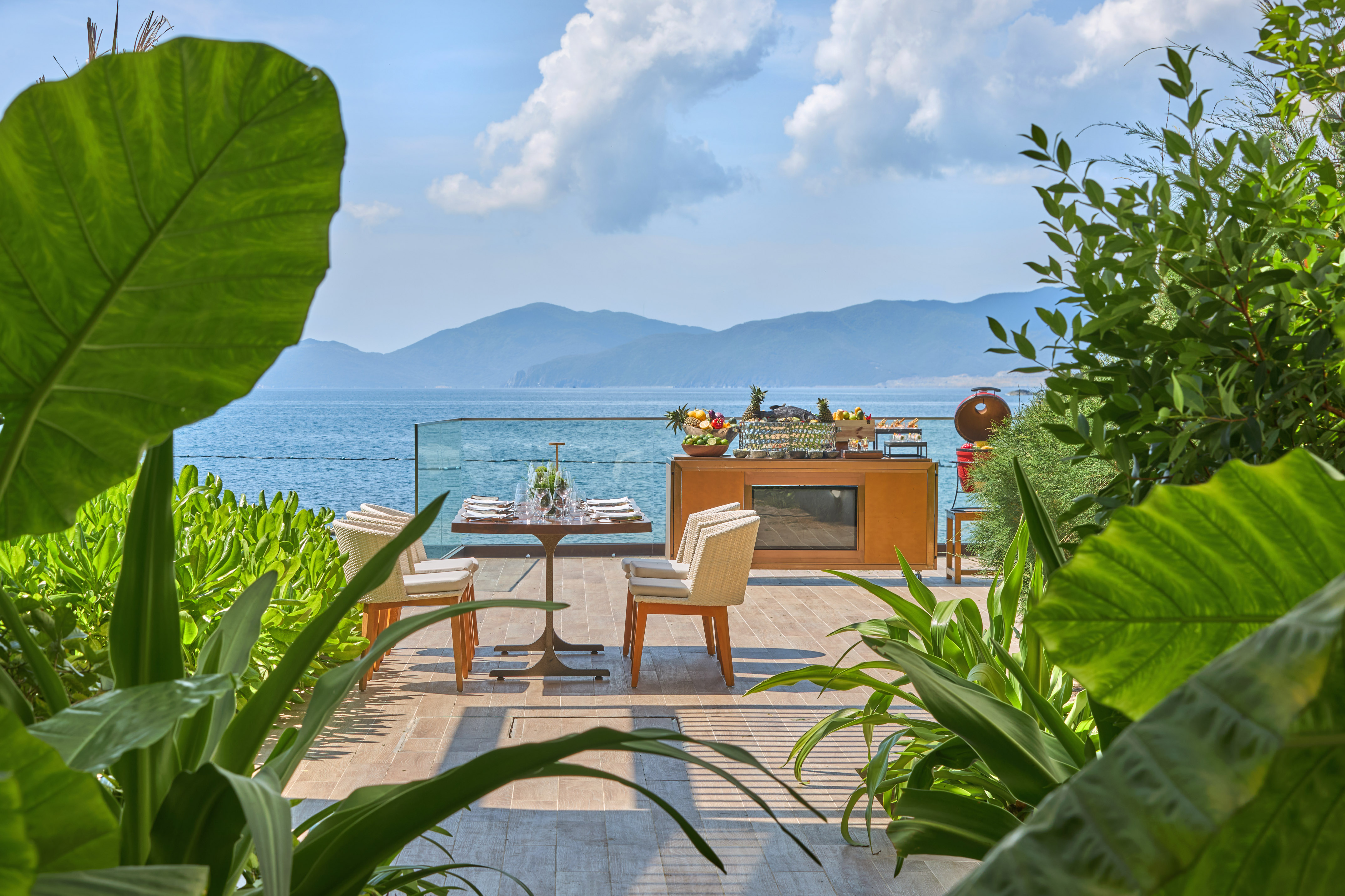 Oceanfront dining terrace with tropical plants, buffet, and mountain view.