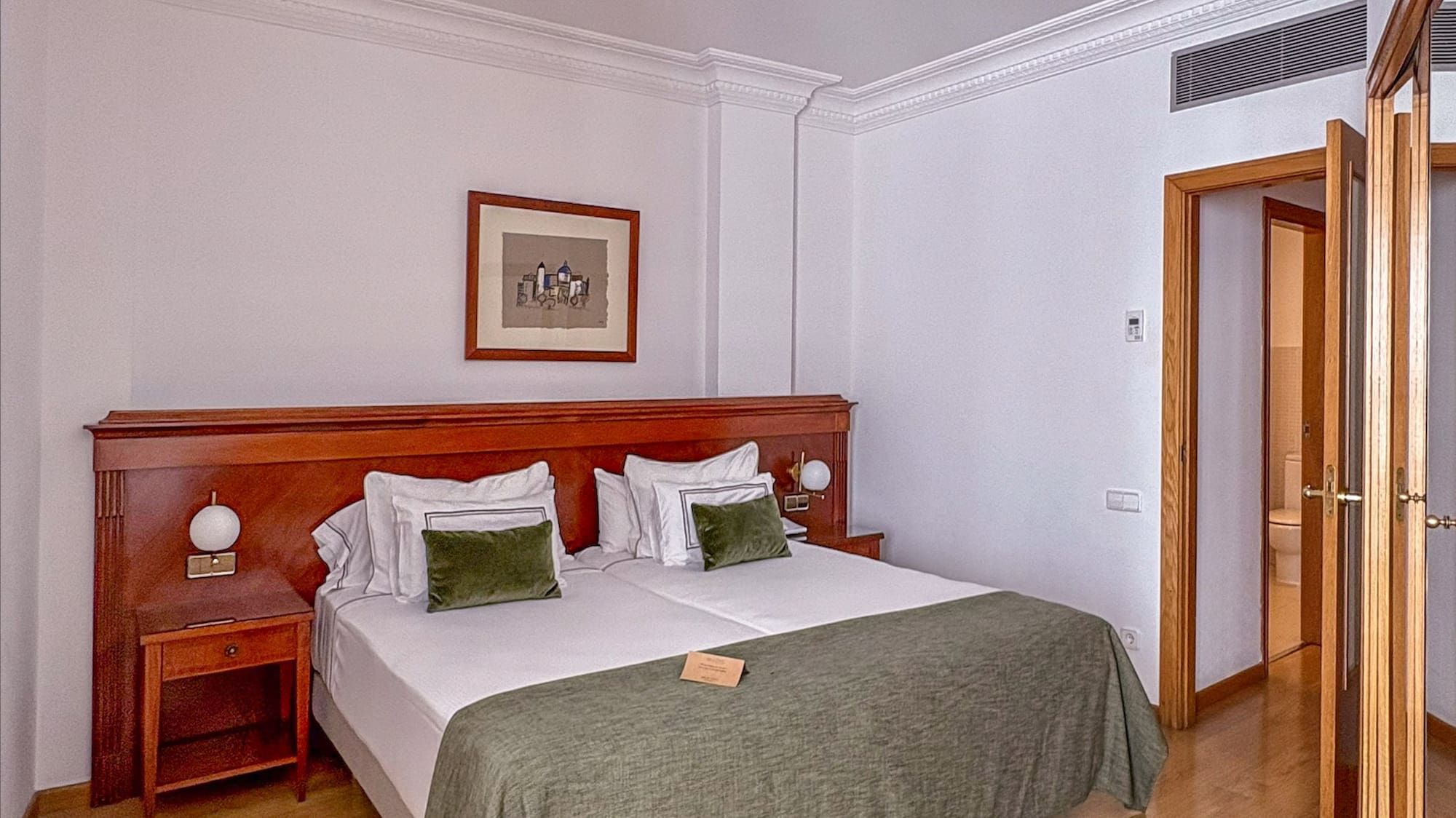 Hotel bedroom with large bed, wooden furniture, green bedding, and wood floor.