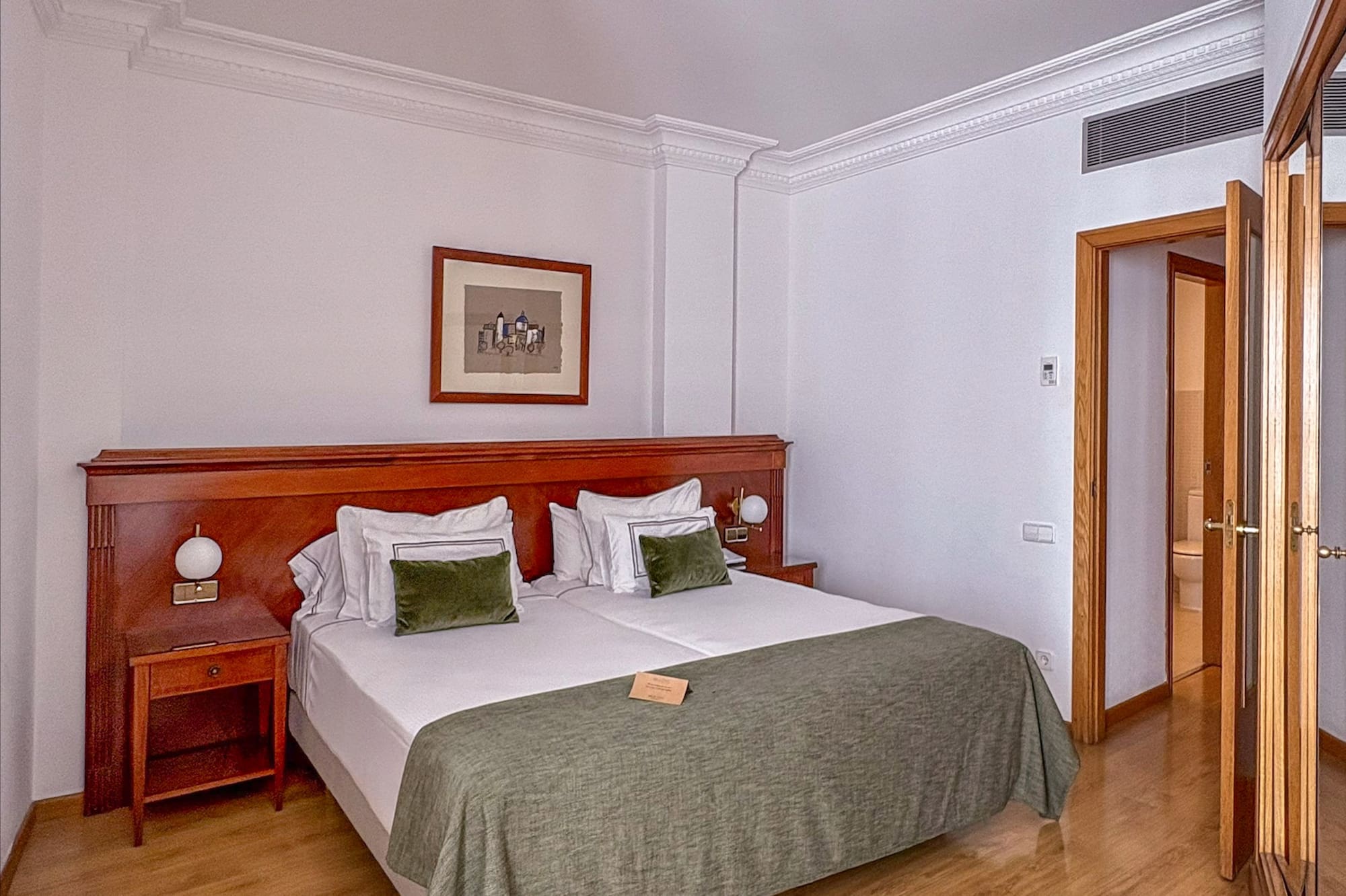 Hotel bedroom with large bed, wooden furniture, green bedding, and wood floor.