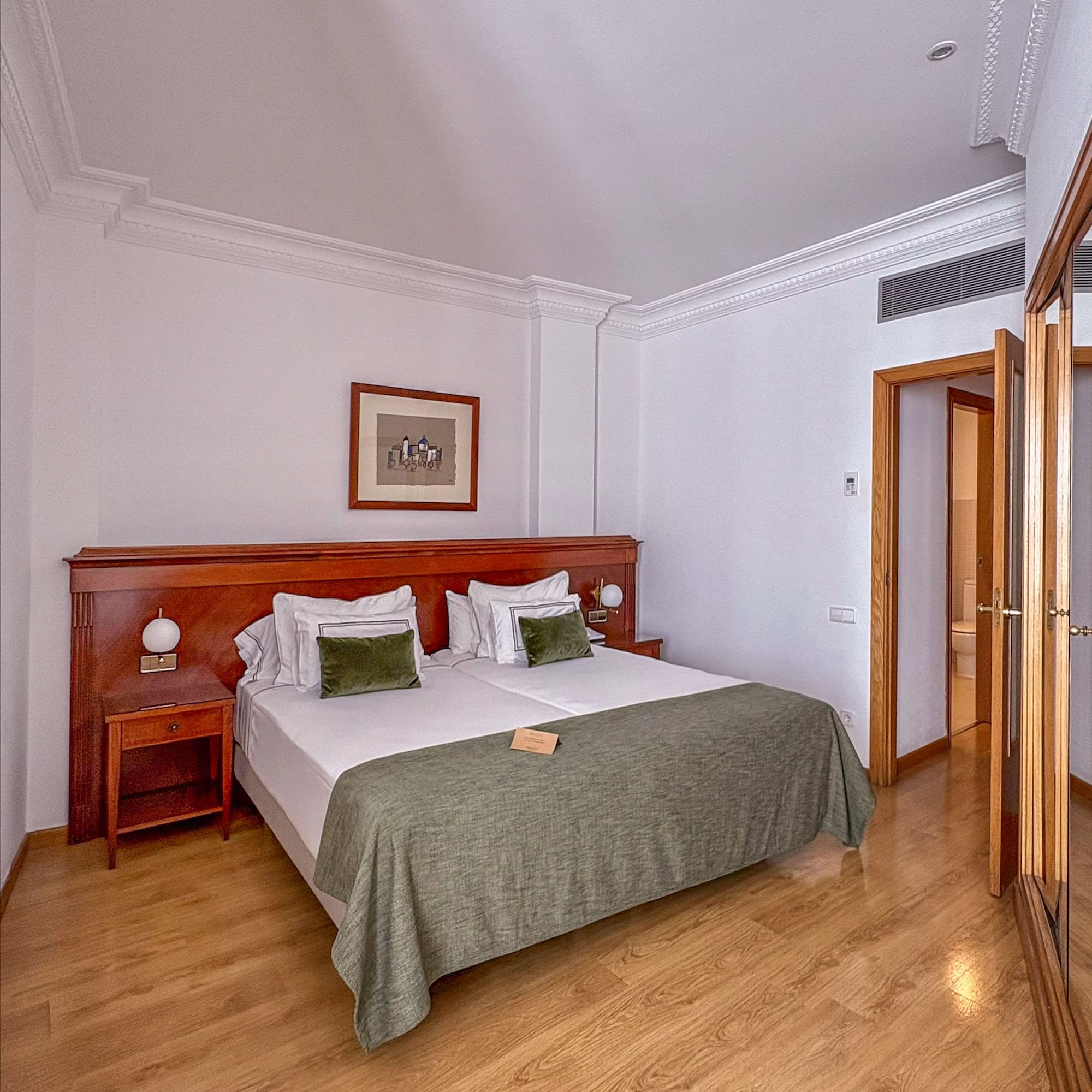 Hotel bedroom with large bed, wooden furniture, green bedding, and wood floor.