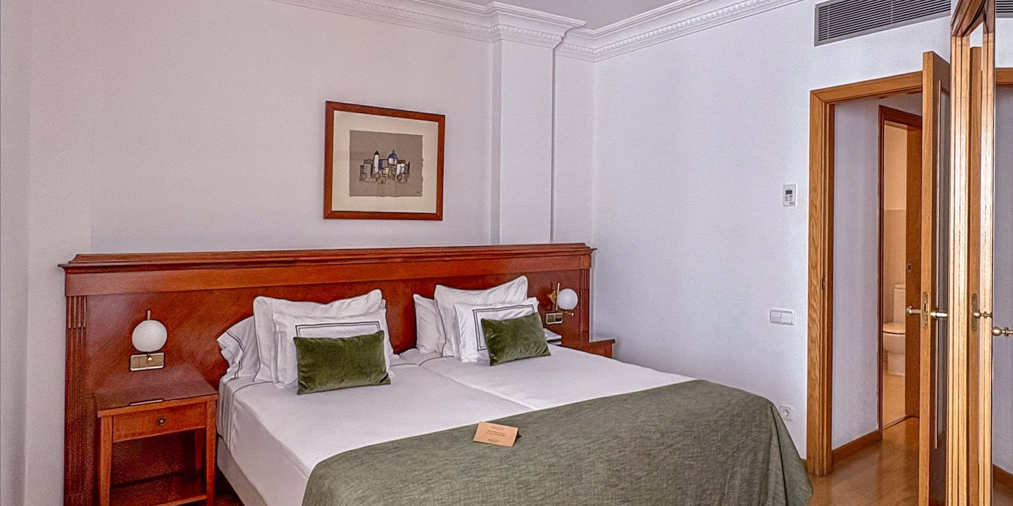 Hotel bedroom with large bed, wooden furniture, green bedding, and wood floor.