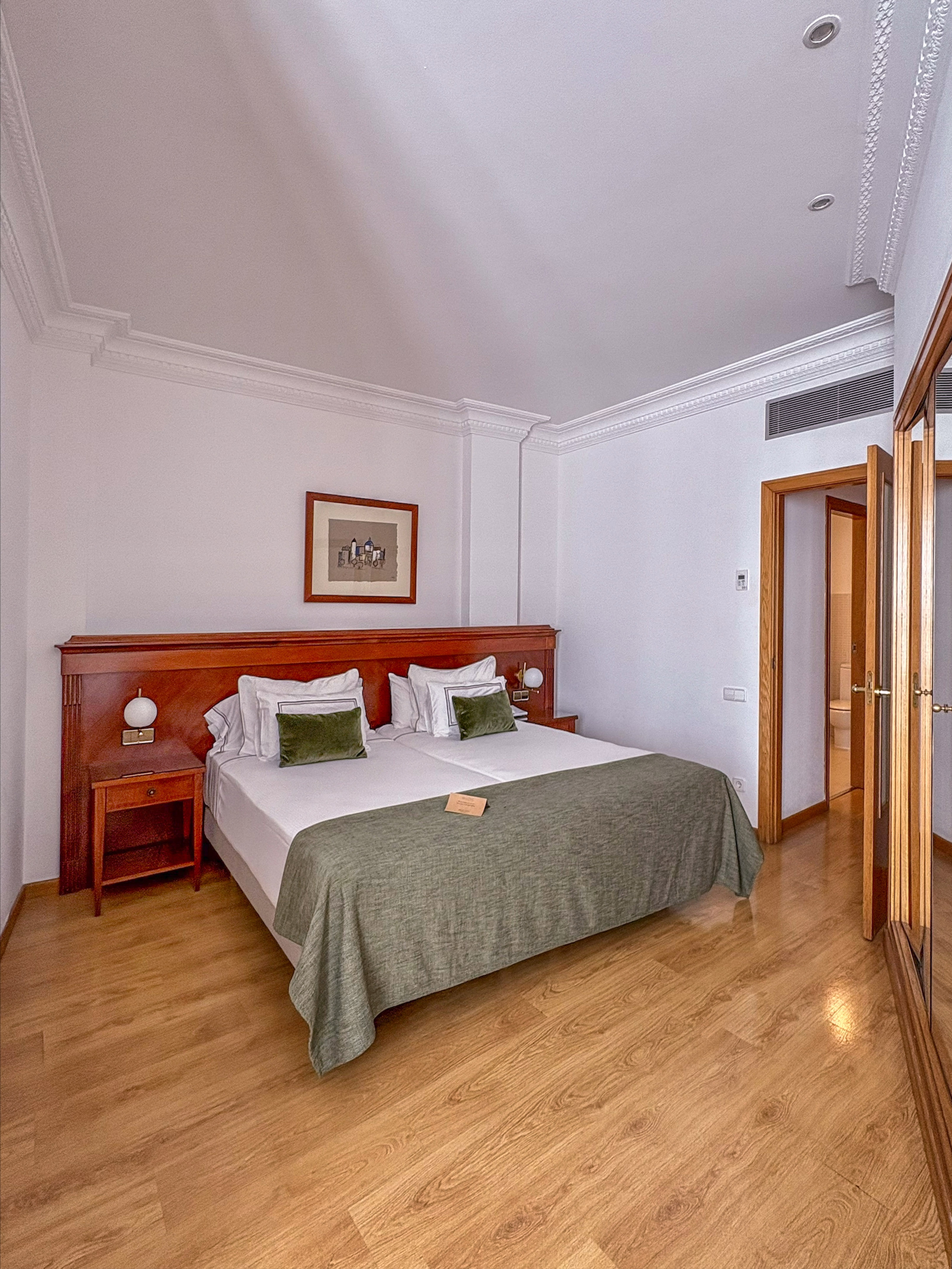 Hotel bedroom with large bed, wooden furniture, green bedding, and wood floor.