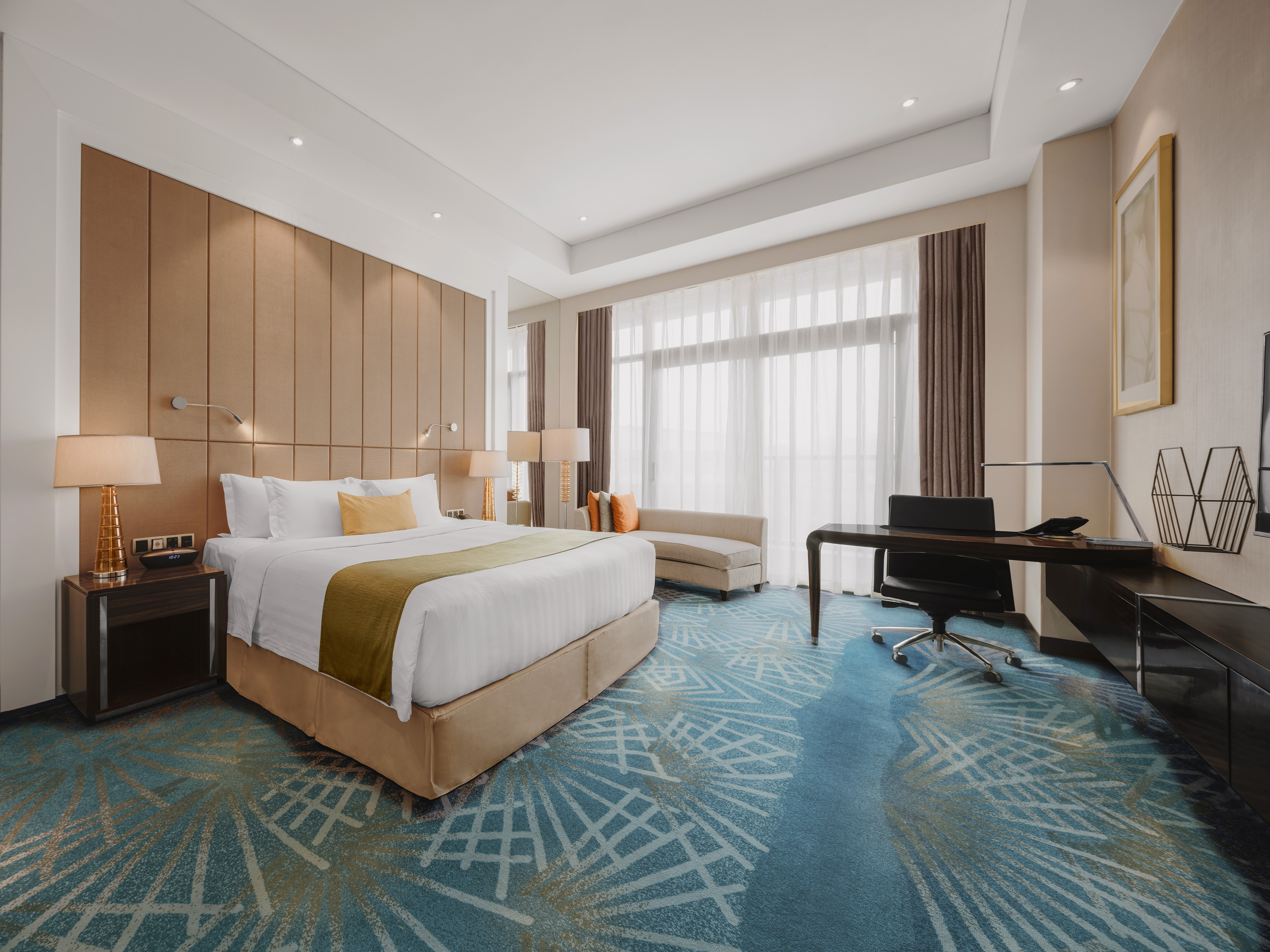 Modern hotel room with king bed, work desk, and blue geometric carpet.