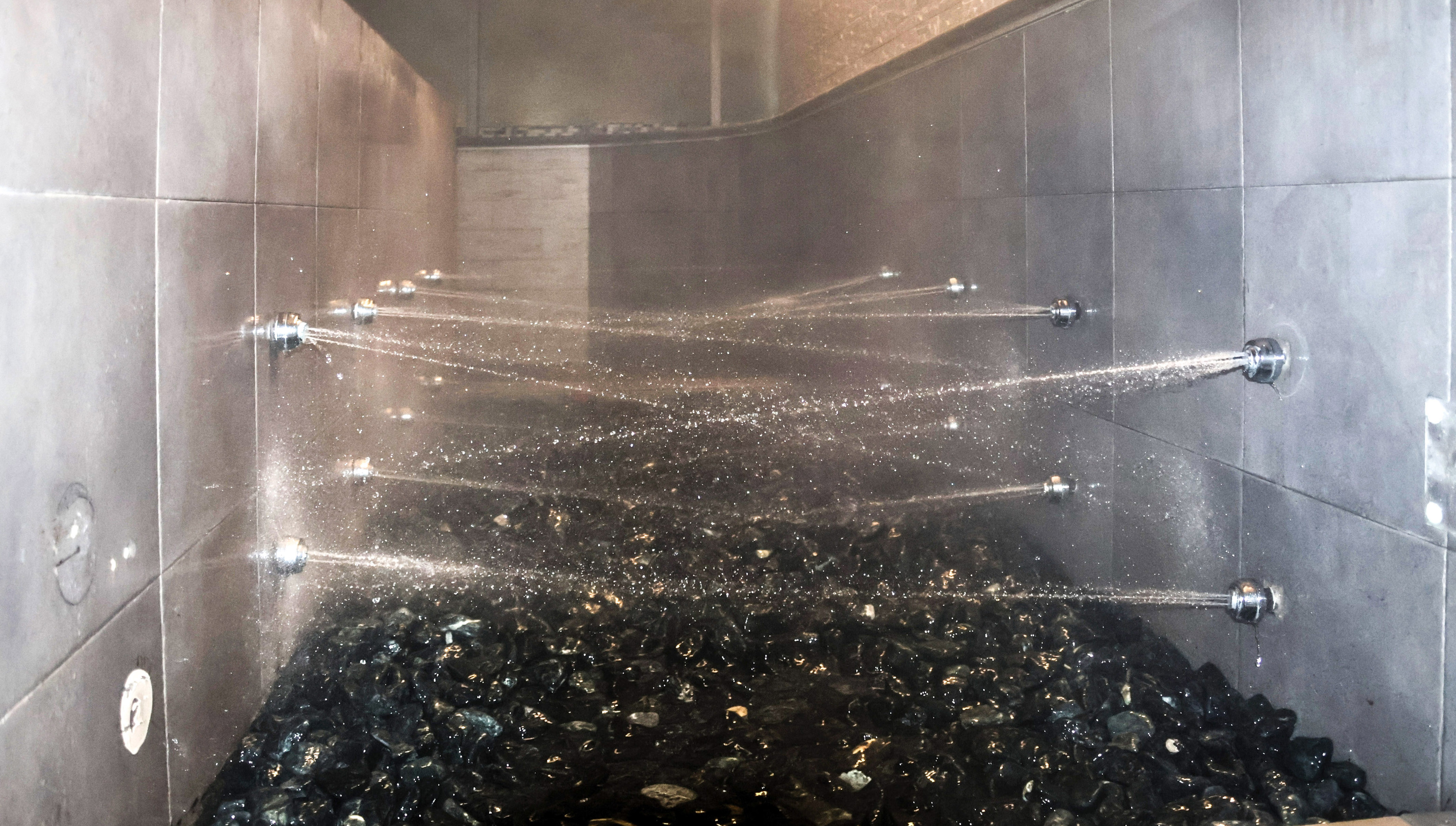 Wellness spa shower with horizontal water jets and black rock bed.