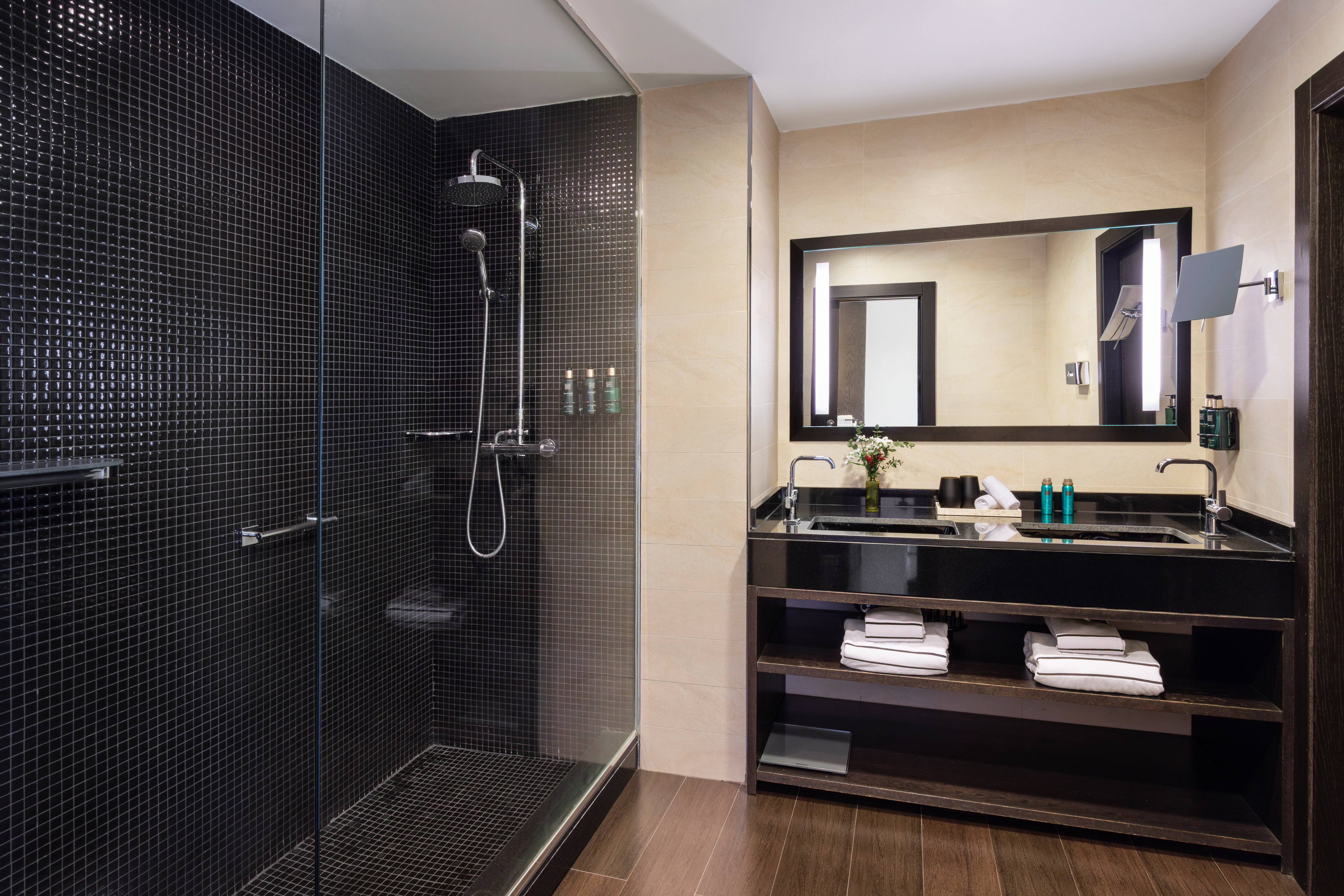 Modern bathroom with walk-in shower, black mosaic tiles, and double vanity.