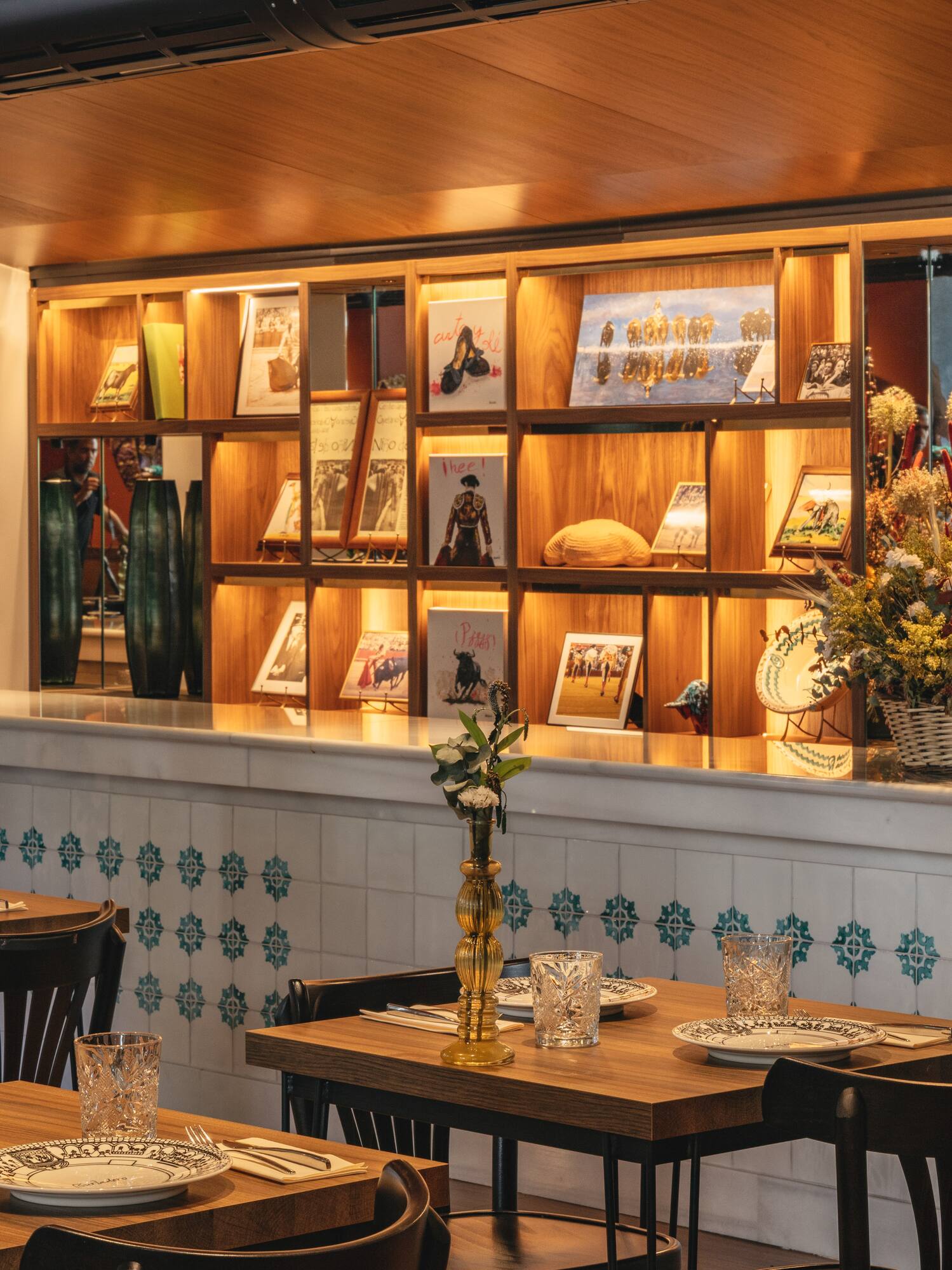 Restaurant interior with set wooden tables, tiled counter, and illuminated display shelves.