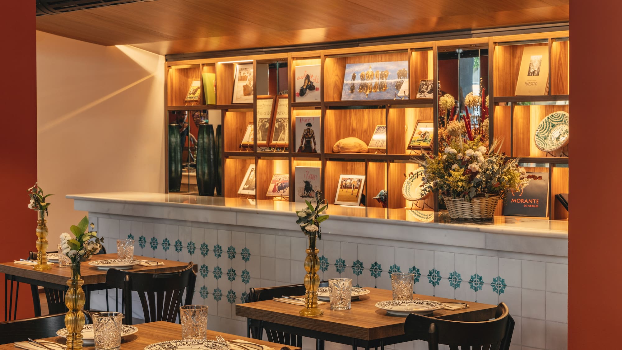Restaurante español con mesas de madera, barra azulejada y estantería iluminada.