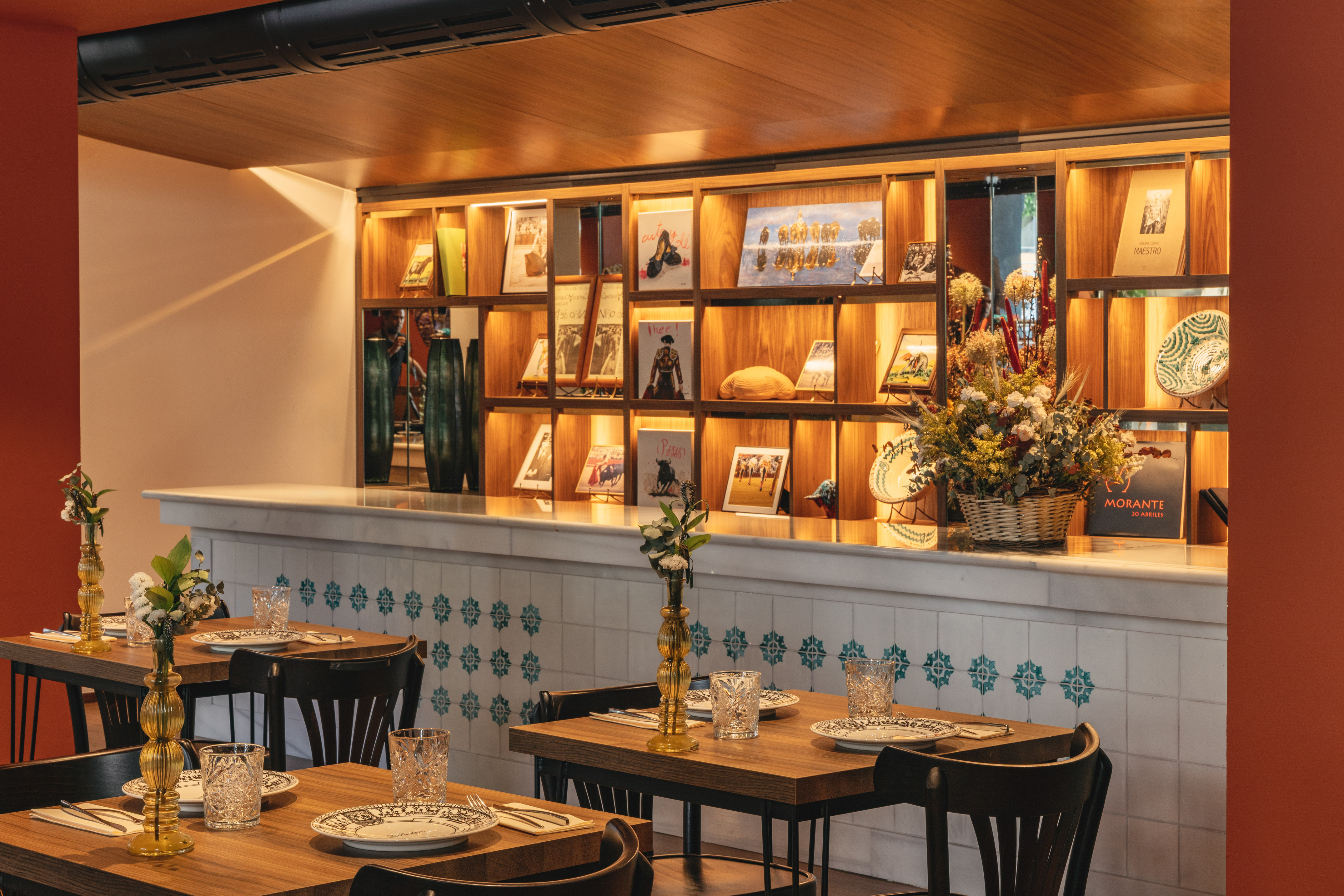Restaurant interior with set wooden tables, tiled counter, and illuminated display shelves.