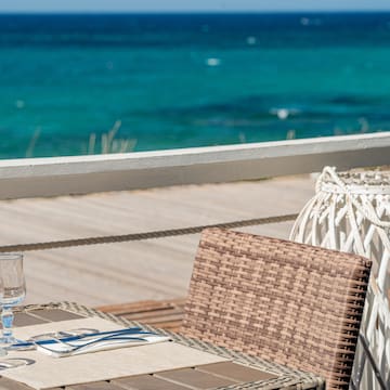 a table with a glass and a chair on a deck overlooking the ocean