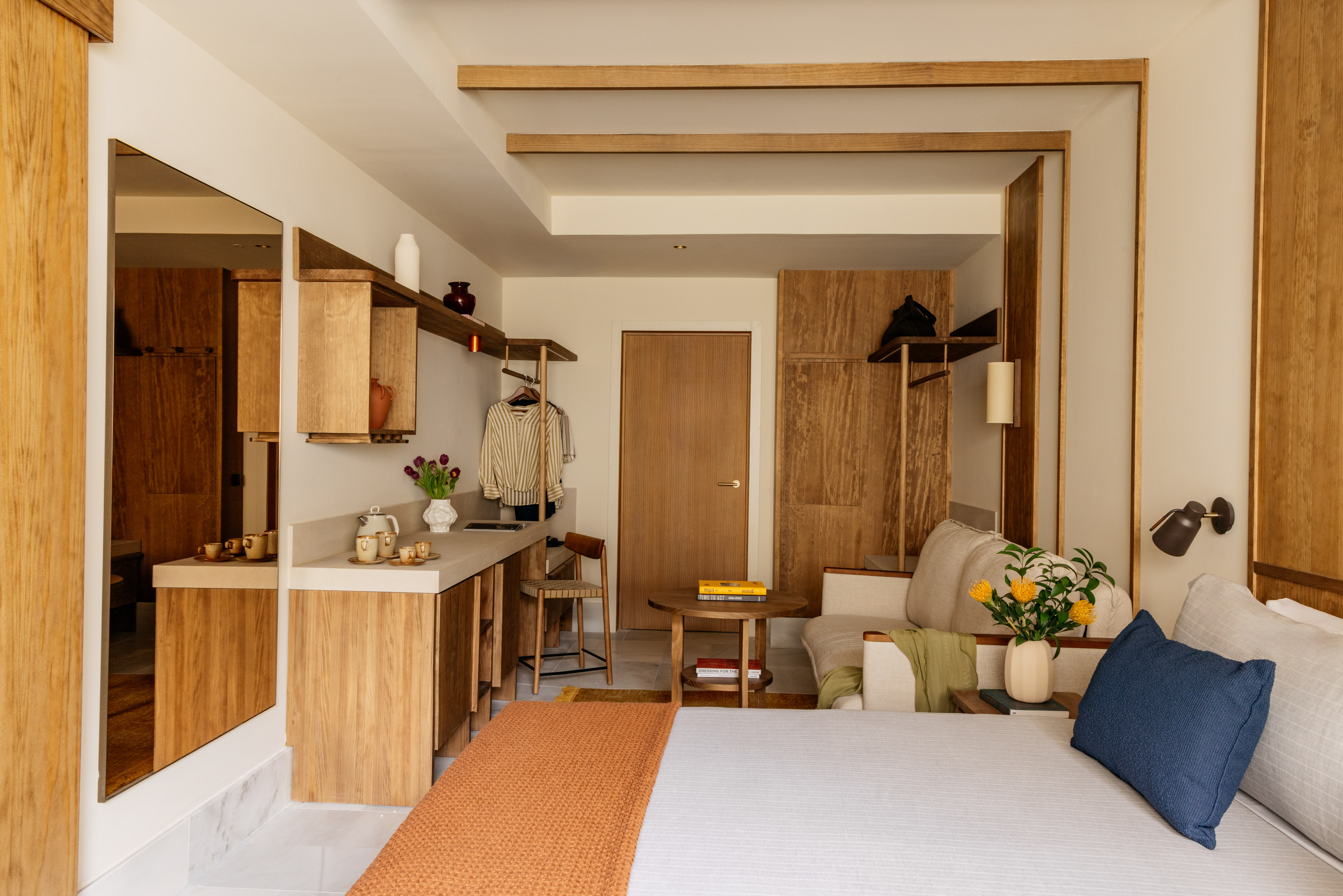 Modern hotel studio with wooden kitchenette, bed, and seating area.