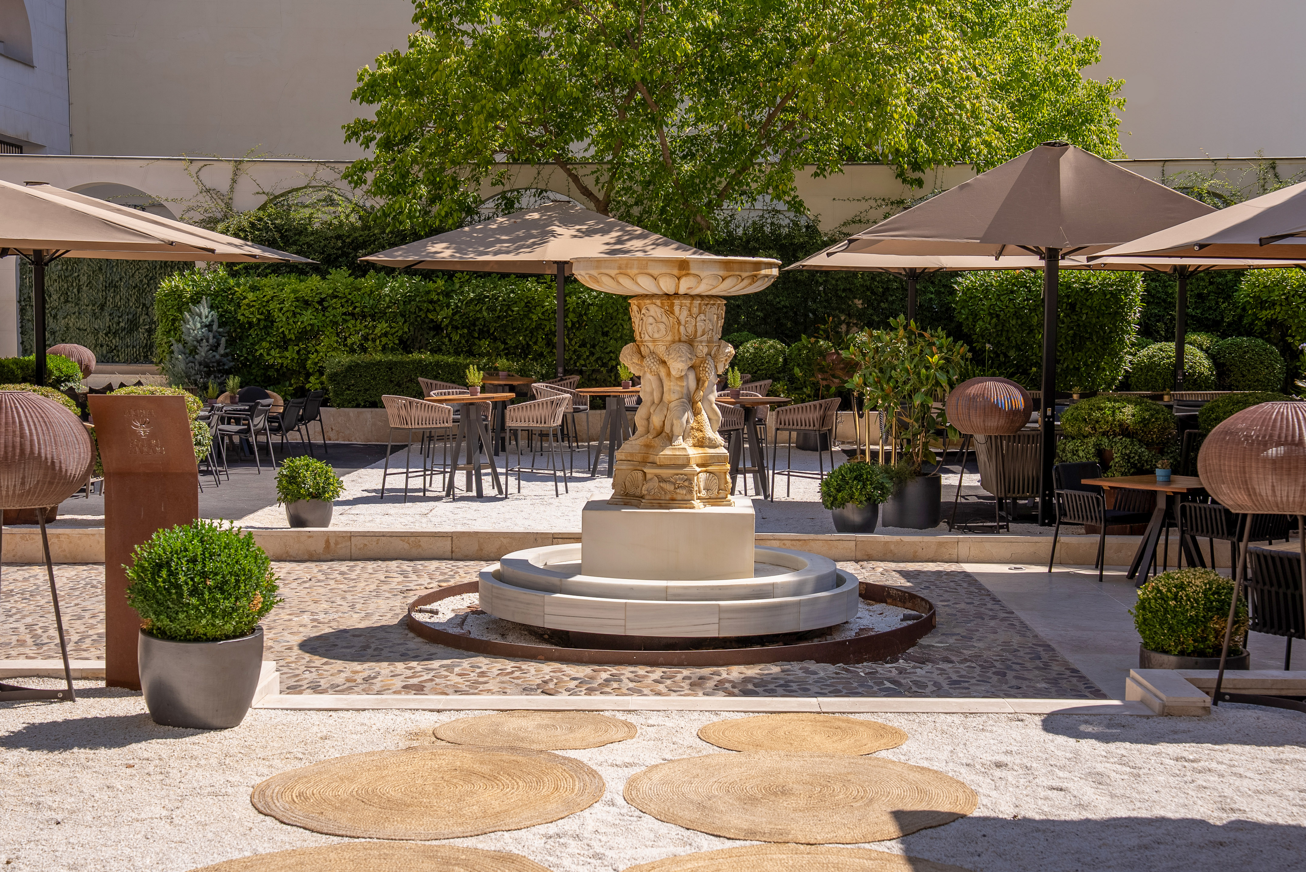 Ornate stone fountain centerpiece in a lush hotel patio with cafe seating.