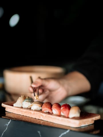a person holding chopsticks to a plate of sushi