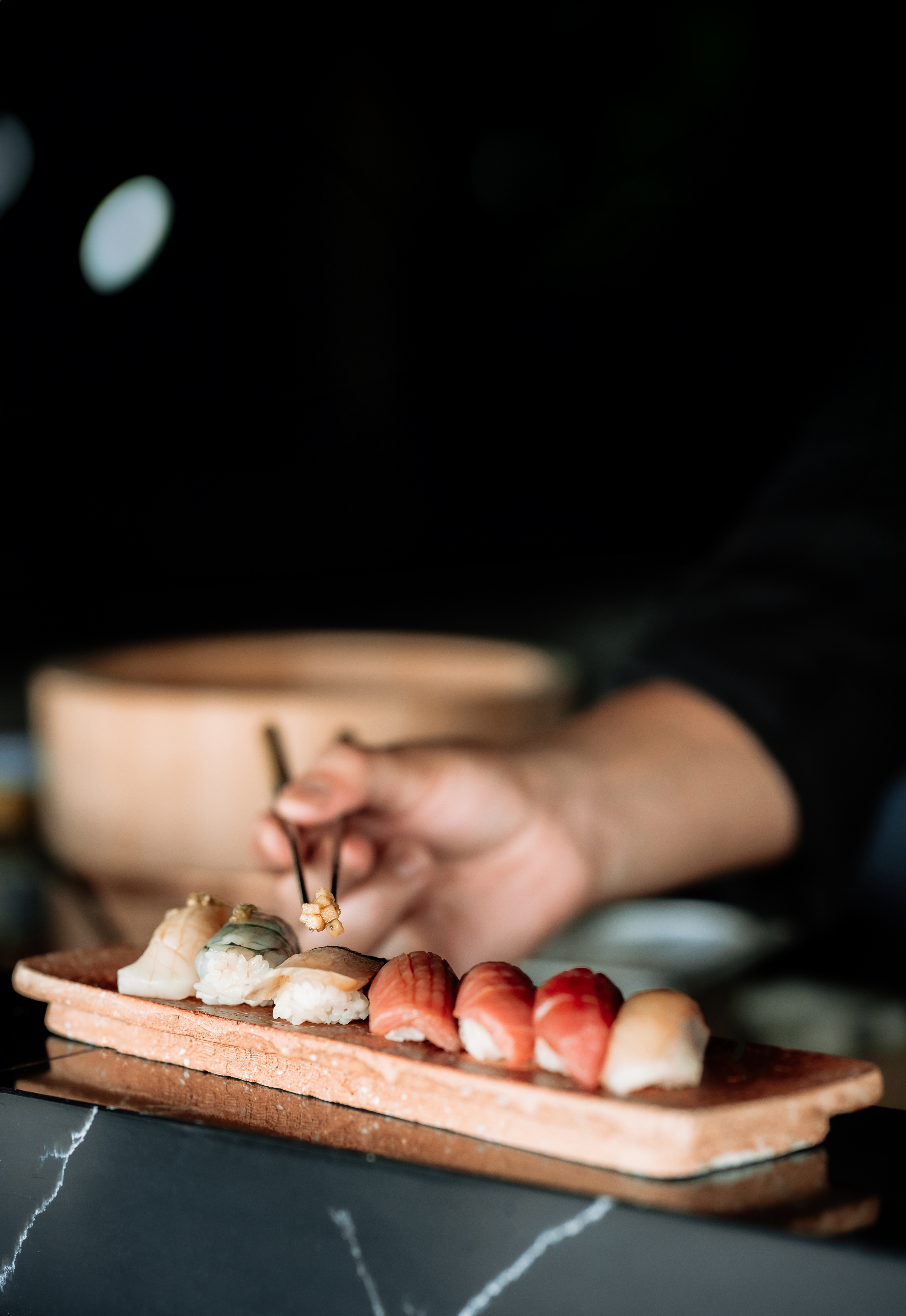 Hand picks fresh assorted nigiri sushi from a rustic wooden plate with chopsticks.
