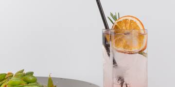 a glass of liquid with a slice of orange and a plate of edamame