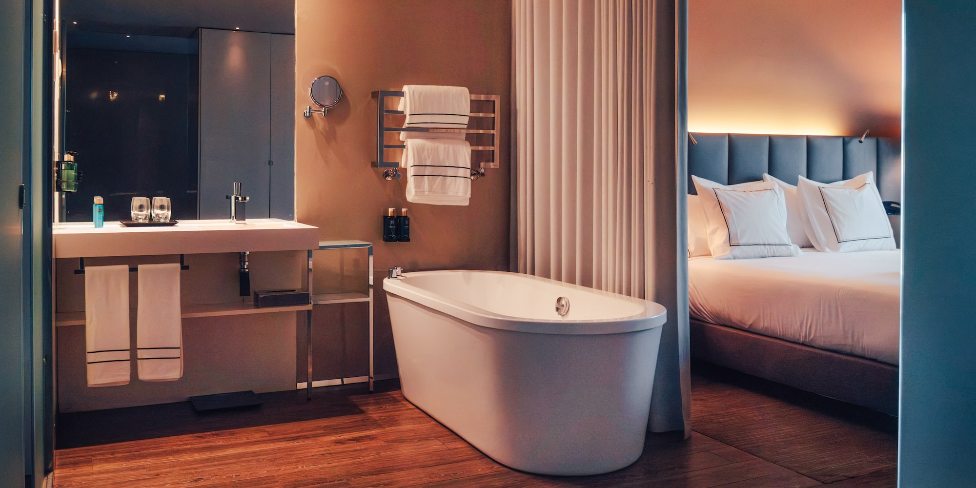 Modern hotel bathroom with freestanding tub and adjoining bedroom.