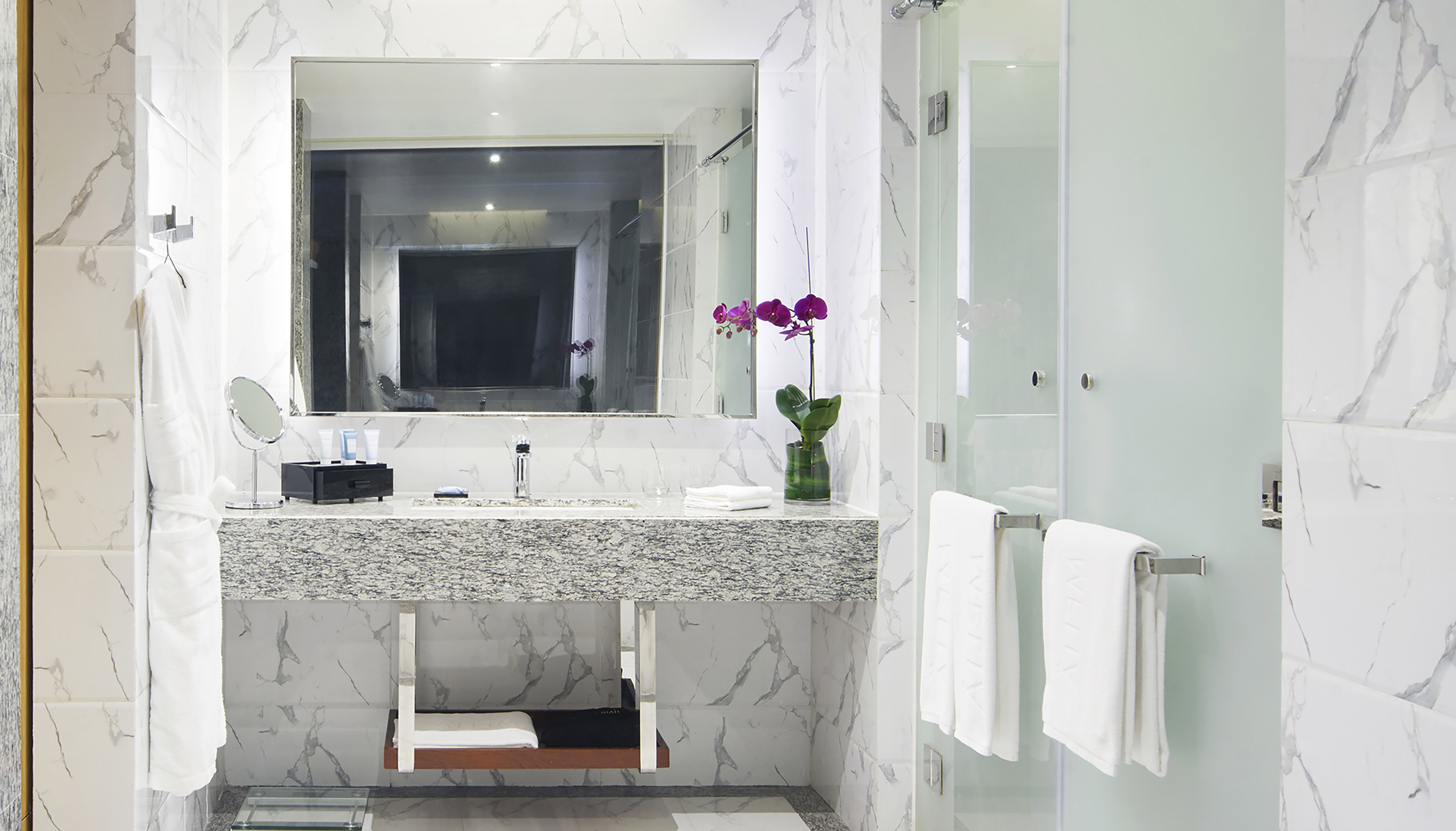 White marble bathroom with granite vanity, purple orchid, and glass shower.