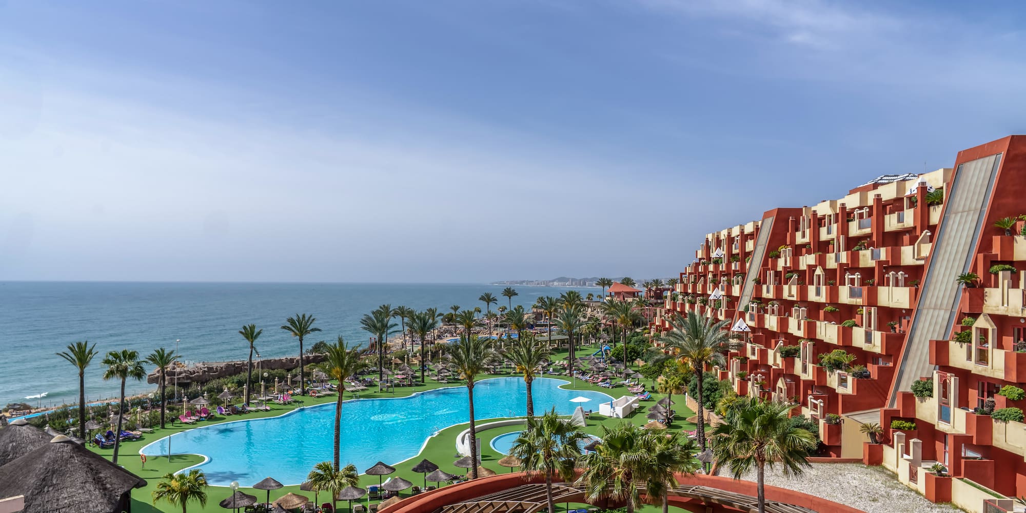 a pool and buildings with palm trees and a body of water