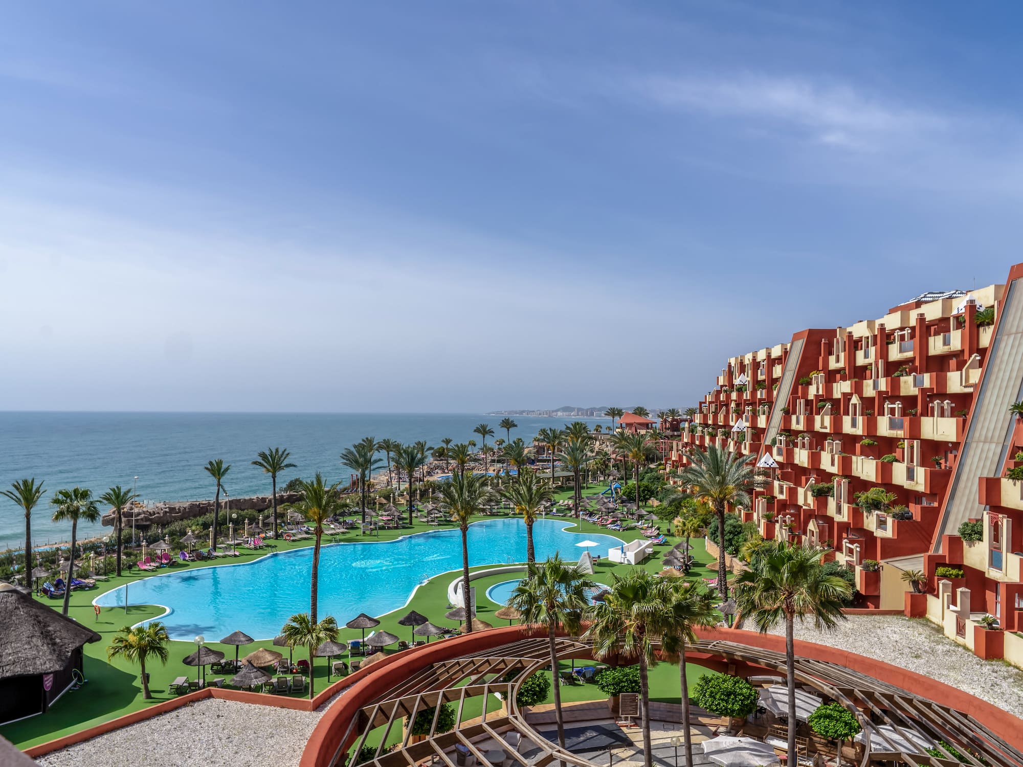 a pool and buildings with palm trees and a body of water