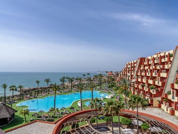 a pool and buildings with palm trees and a body of water