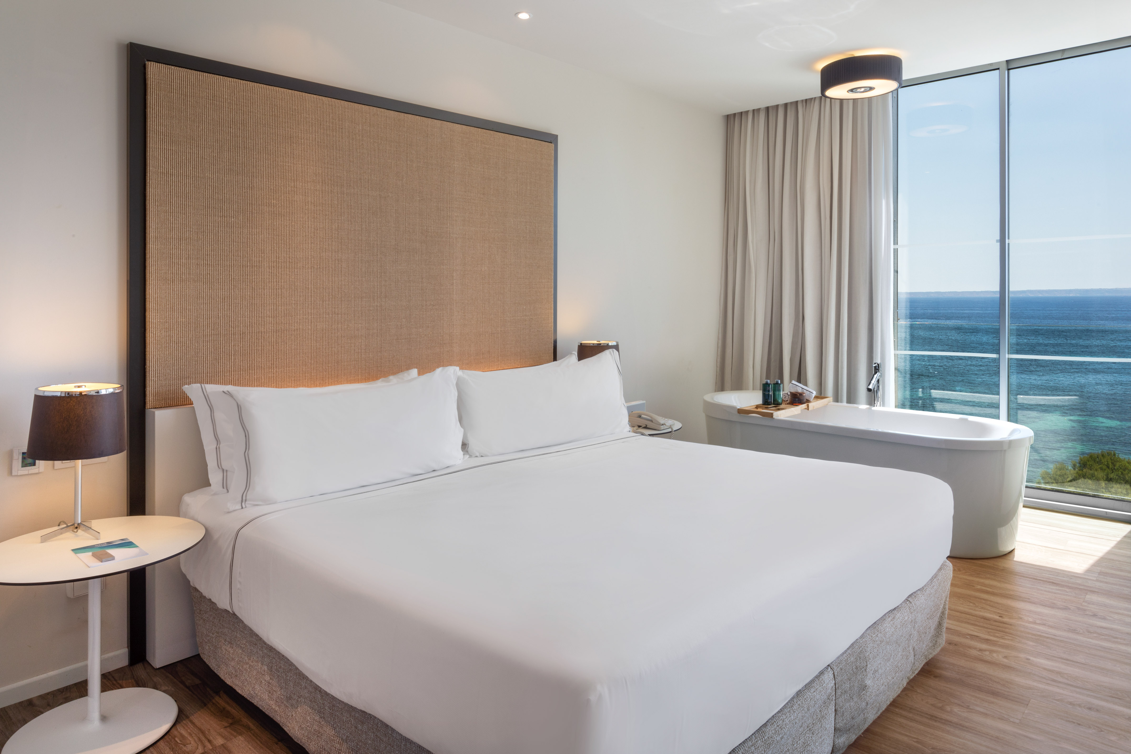 Luxury hotel bedroom with ocean view, king bed, and modern soaking tub.
