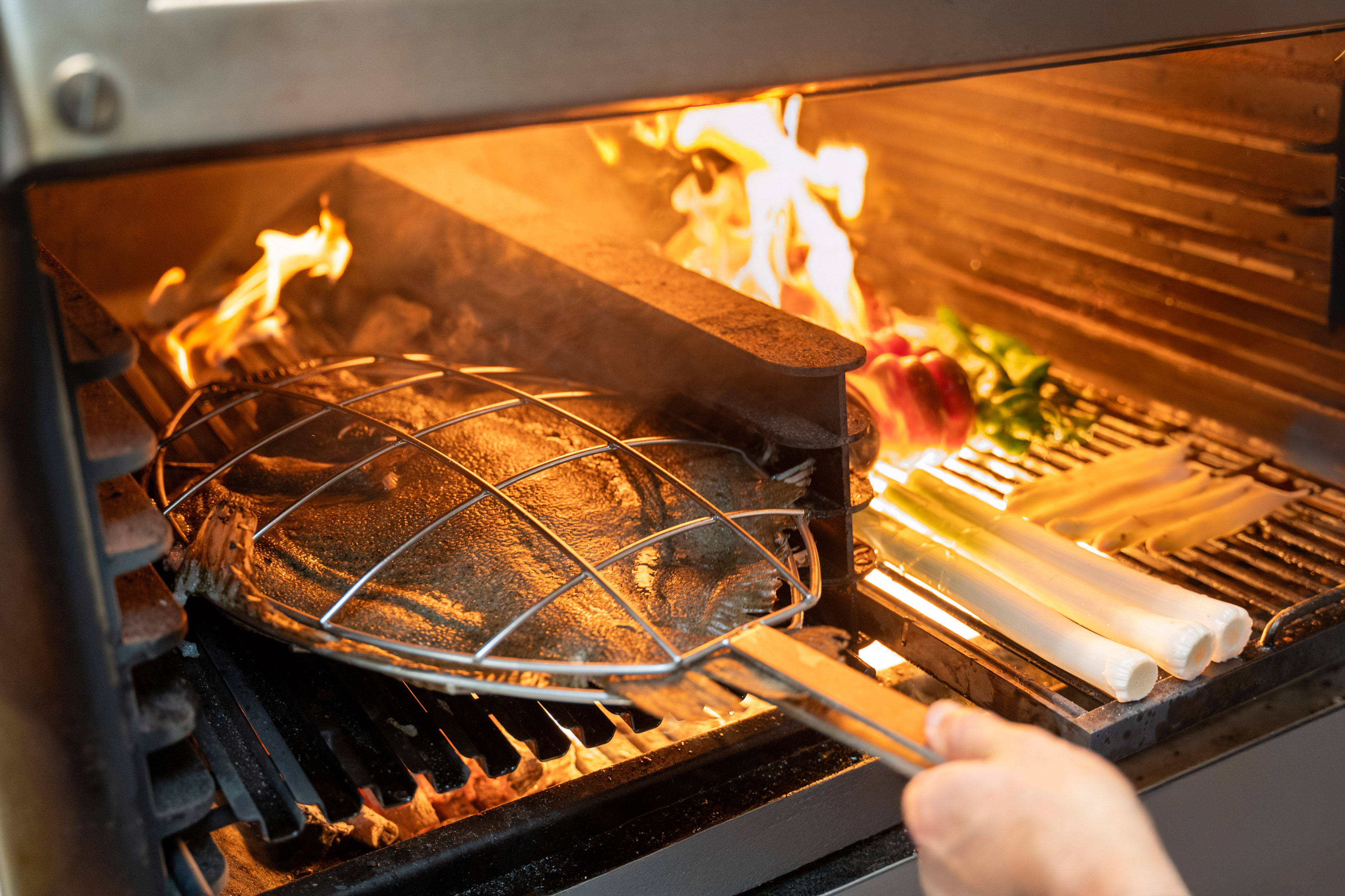 Grilling whole turbot and vegetables in a basket over hot flames.
