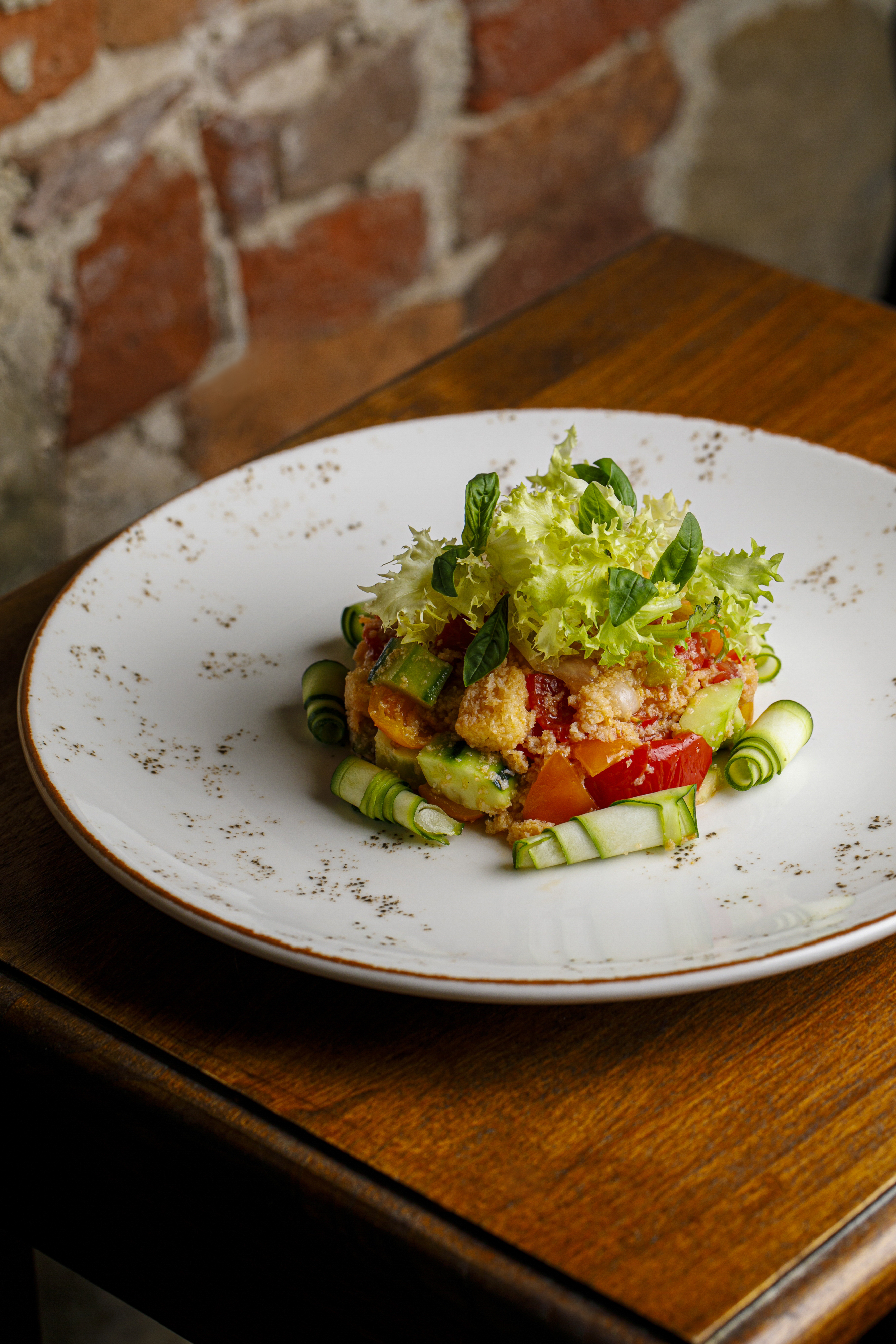 Fresh couscous salad with tomato, zucchini, lettuce, and basil on a white plate.