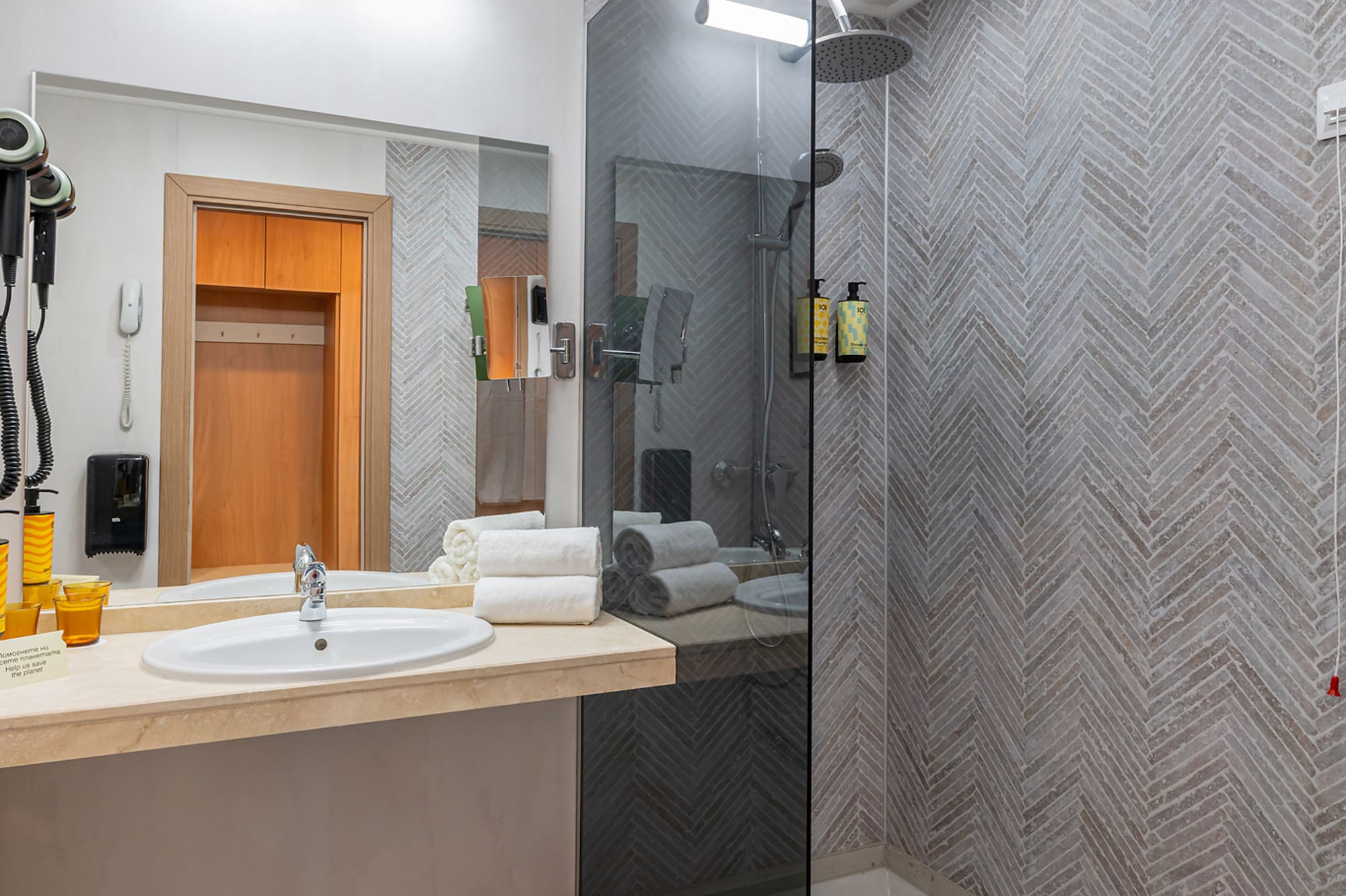 Clean modern bathroom with vanity, glass walk-in shower, and herringbone tiled walls.