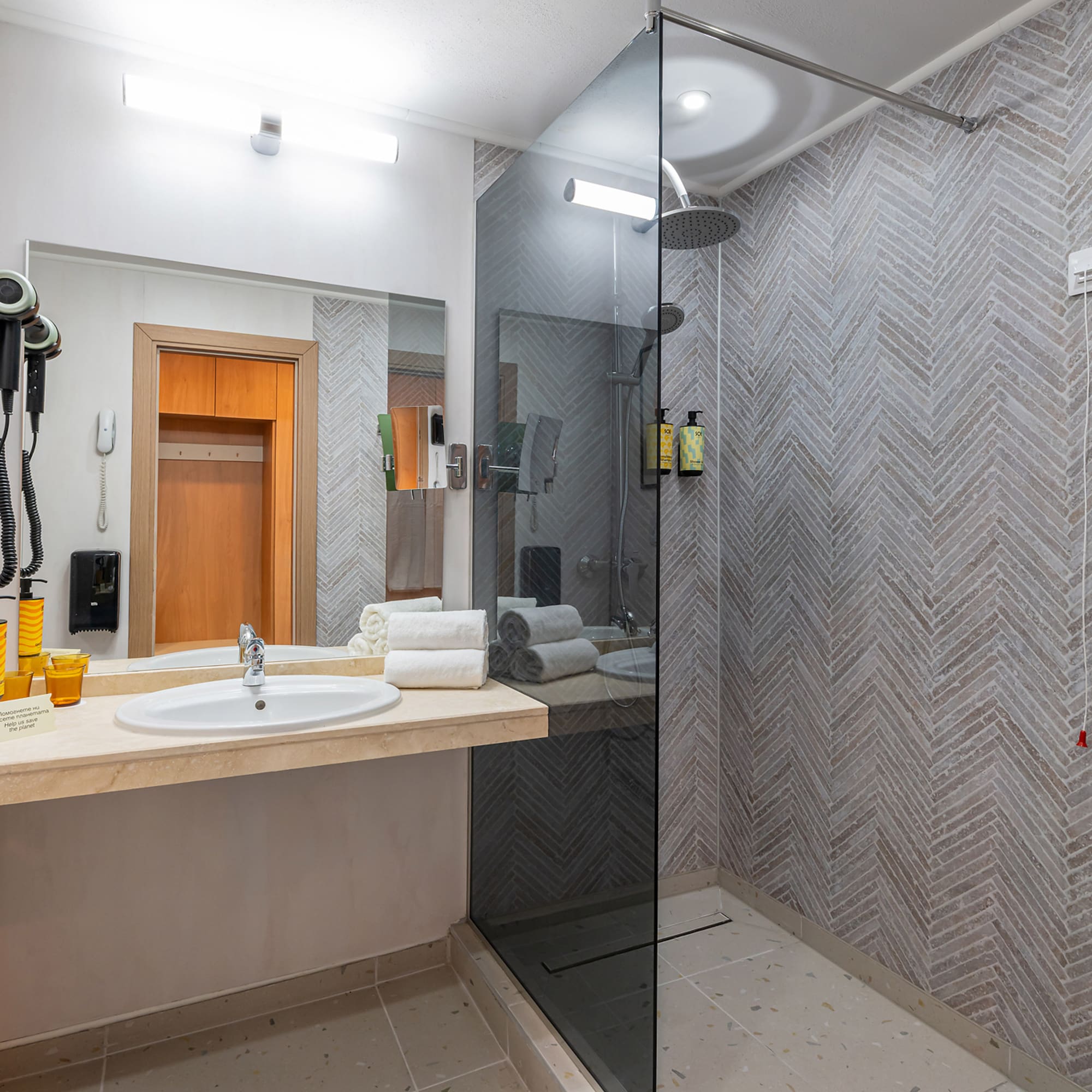 Clean modern bathroom with vanity, glass walk-in shower, and herringbone tiled walls.