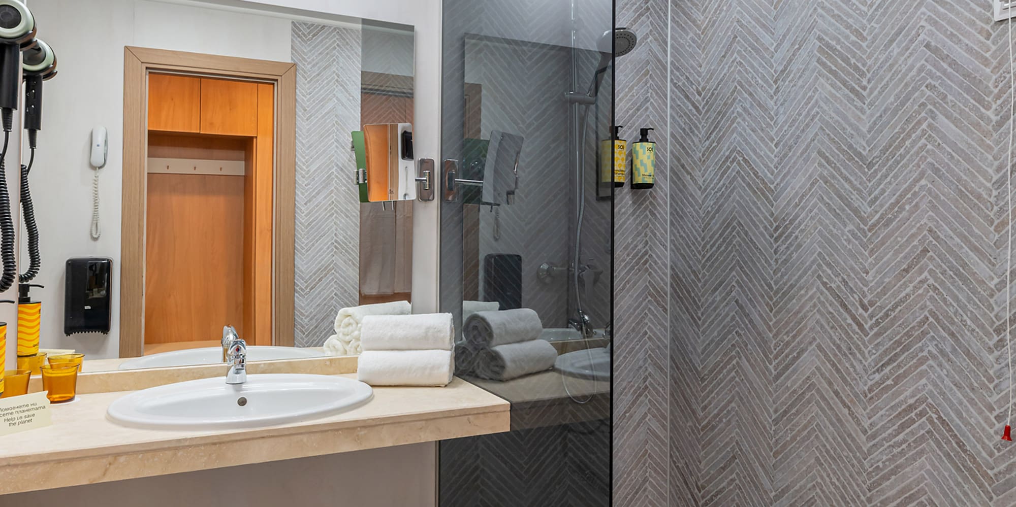 Clean modern bathroom with vanity, glass walk-in shower, and herringbone tiled walls.