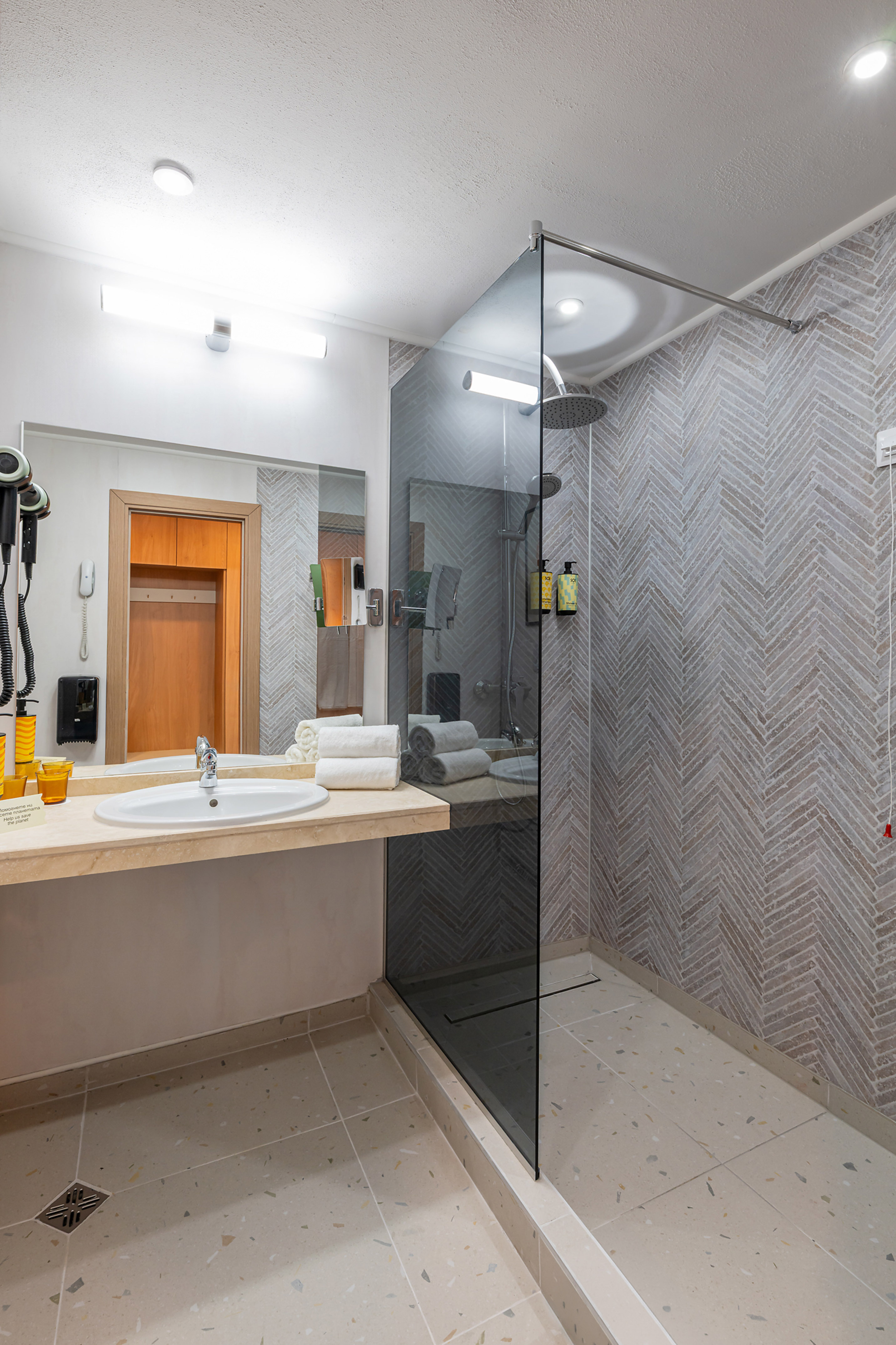 Clean modern bathroom with vanity, glass walk-in shower, and herringbone tiled walls.