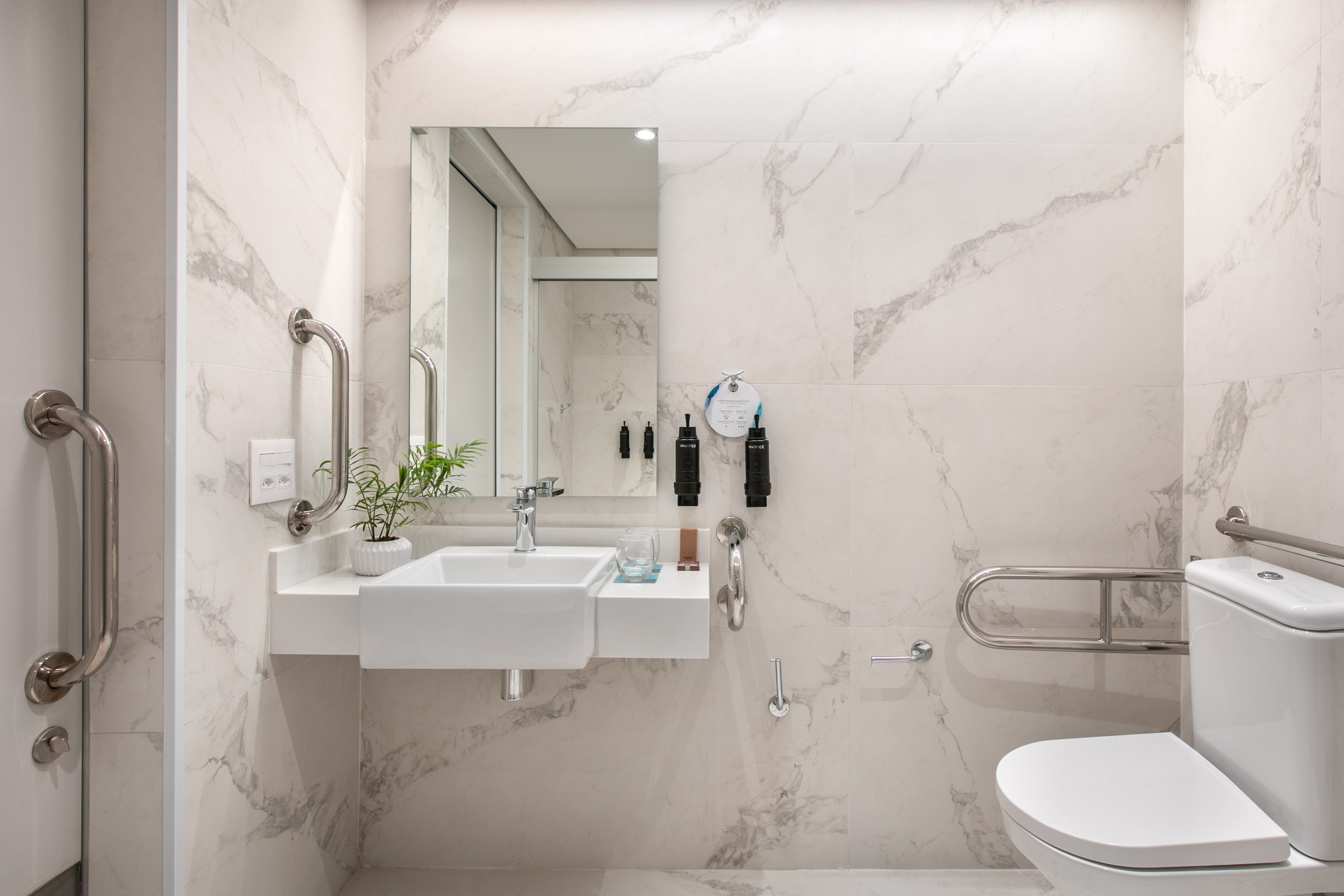 Modern accessible bathroom with marble walls, floating sink, toilet, and grab bars.