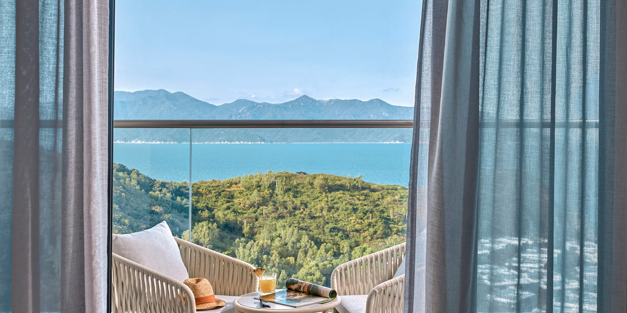 Balcony with sea view, outdoor seating, green hills, and blue sky.