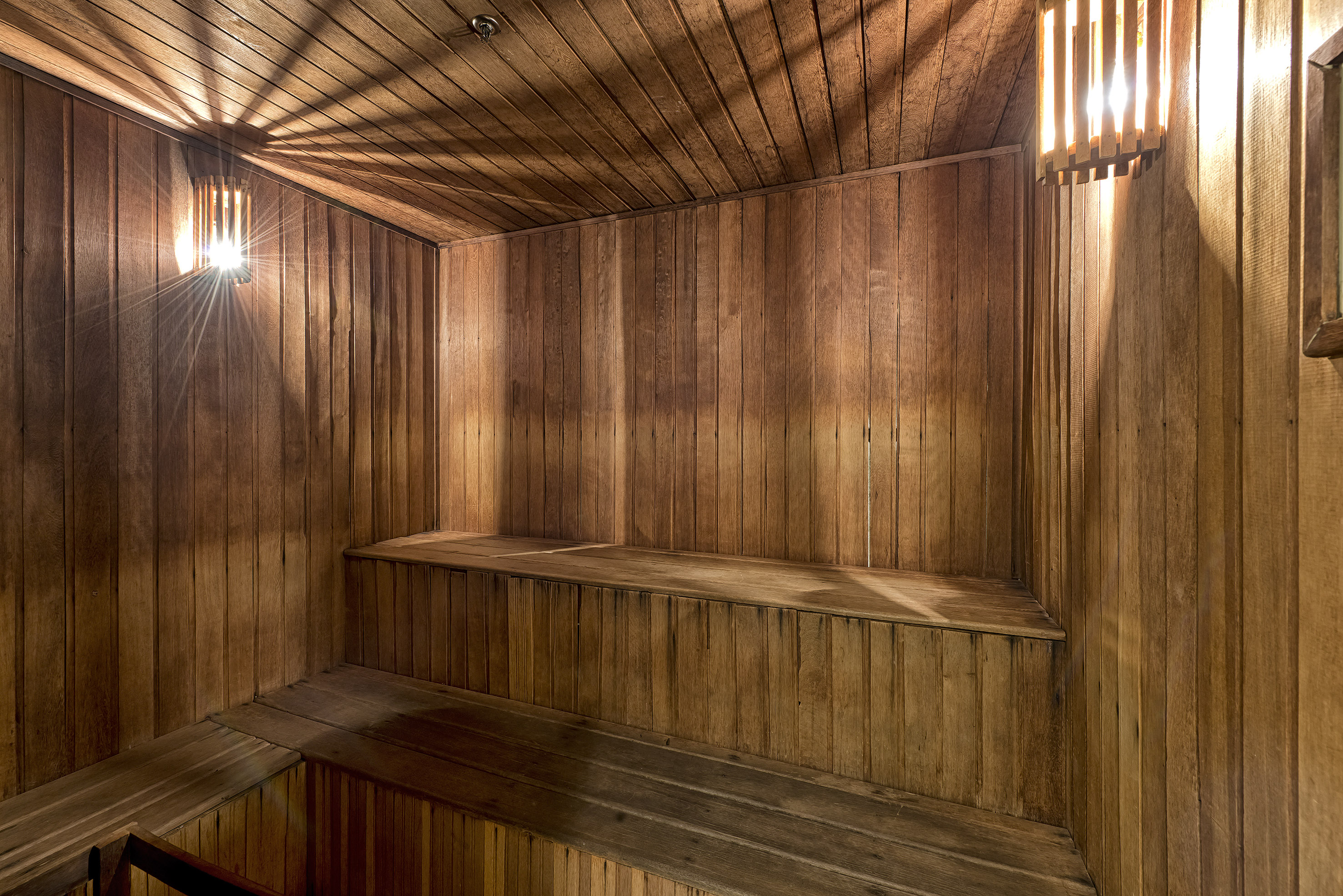 Wooden sauna interior with benches, slatted walls, and warm light fixtures.